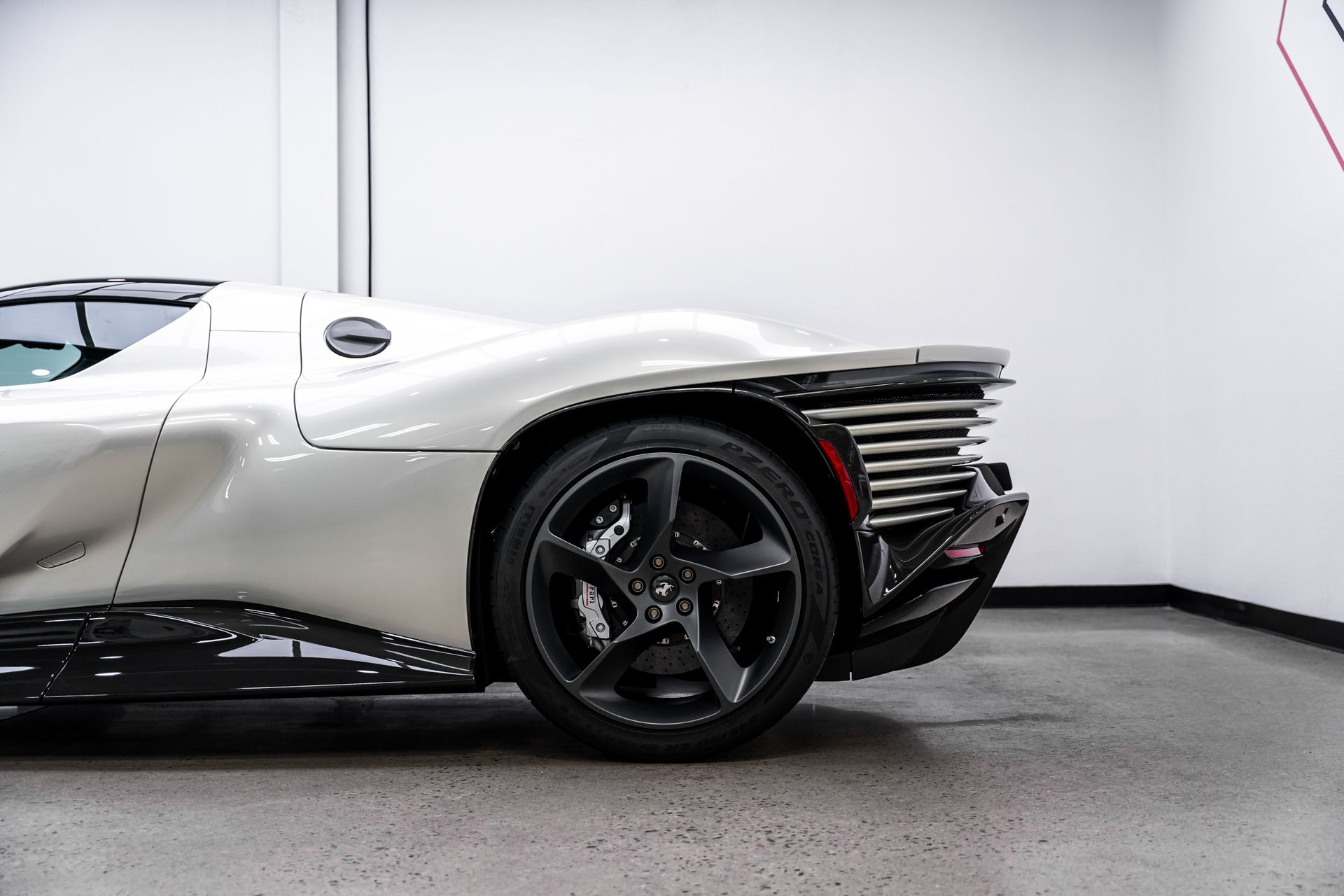 White sports car's rear side, showing a black wheel, aerodynamic design, and taillight.