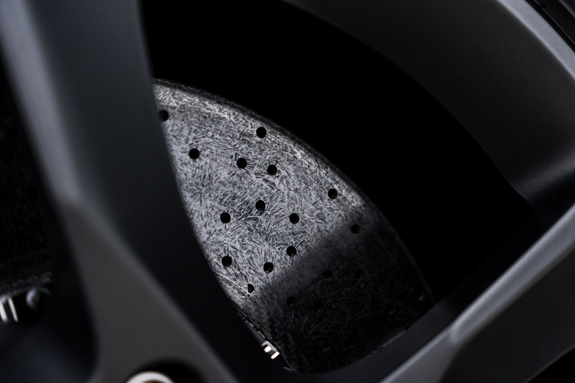 Black car brake disc with drilled holes.