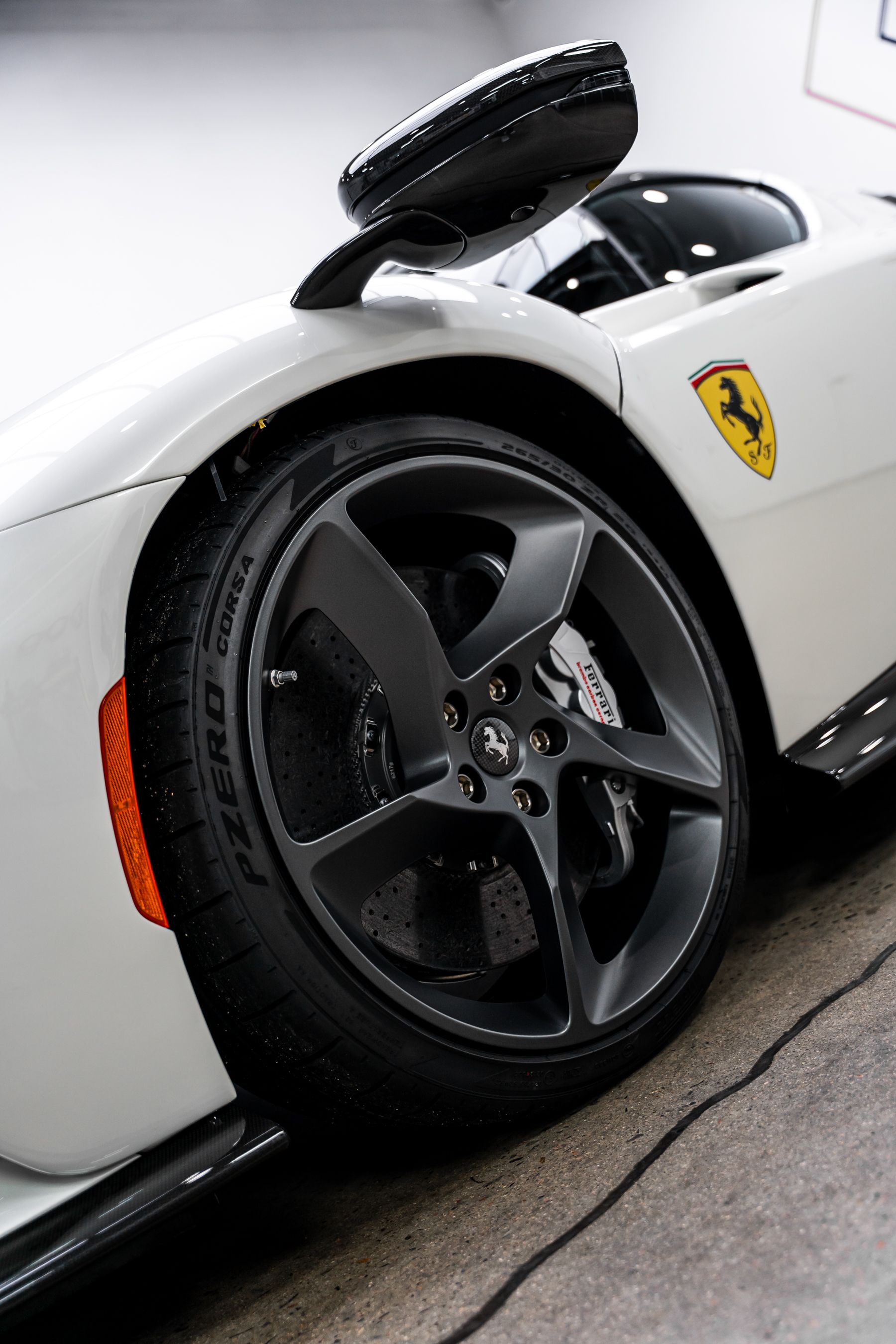 White Ferrari sports car wheel, black rim, tire, side mirror, and Ferrari logo.