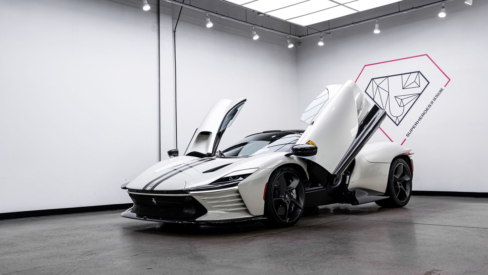 White sports car with doors open, in a gallery setting. A logo of a diamond is visible in the background.