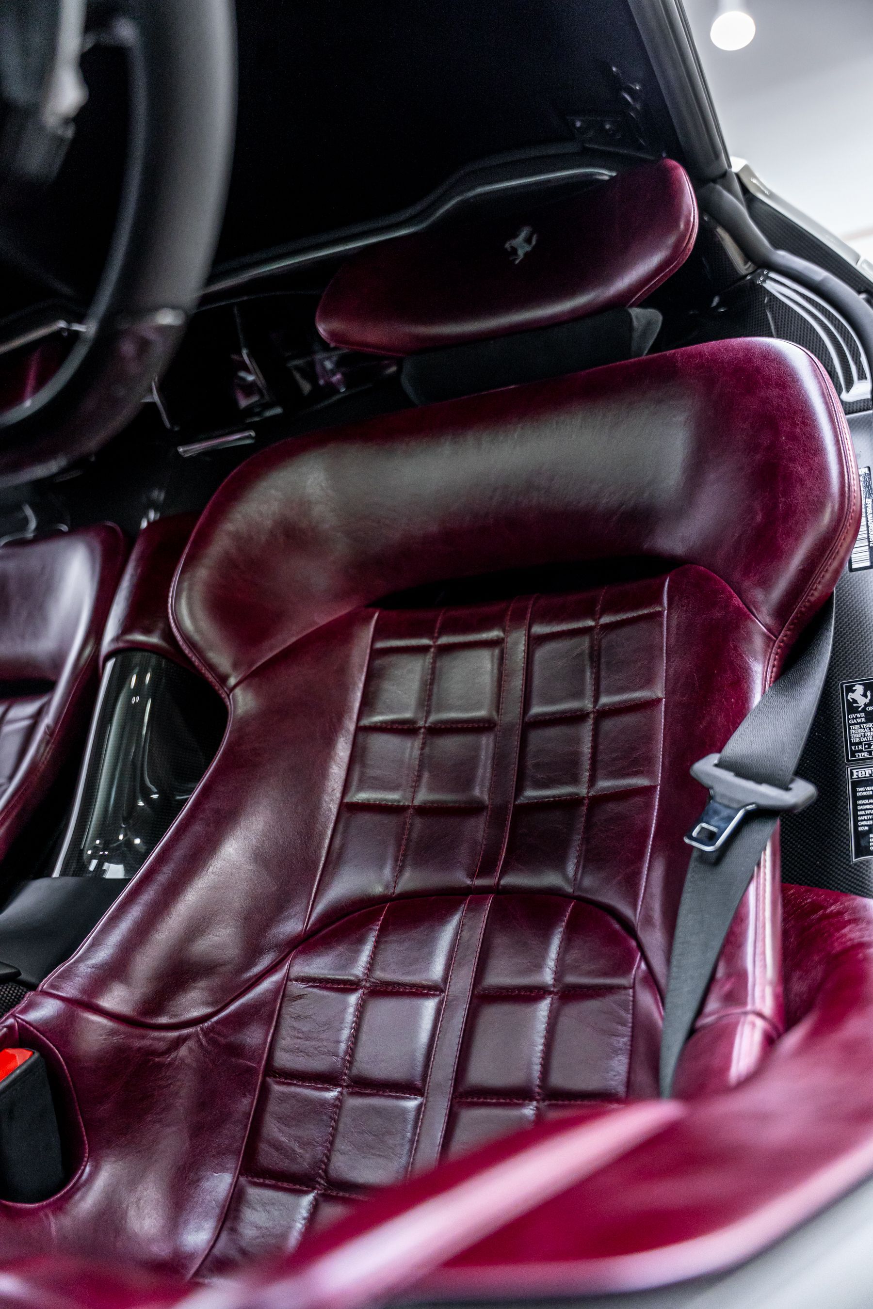 Maroon quilted leather car seat with headrest and black seatbelt.