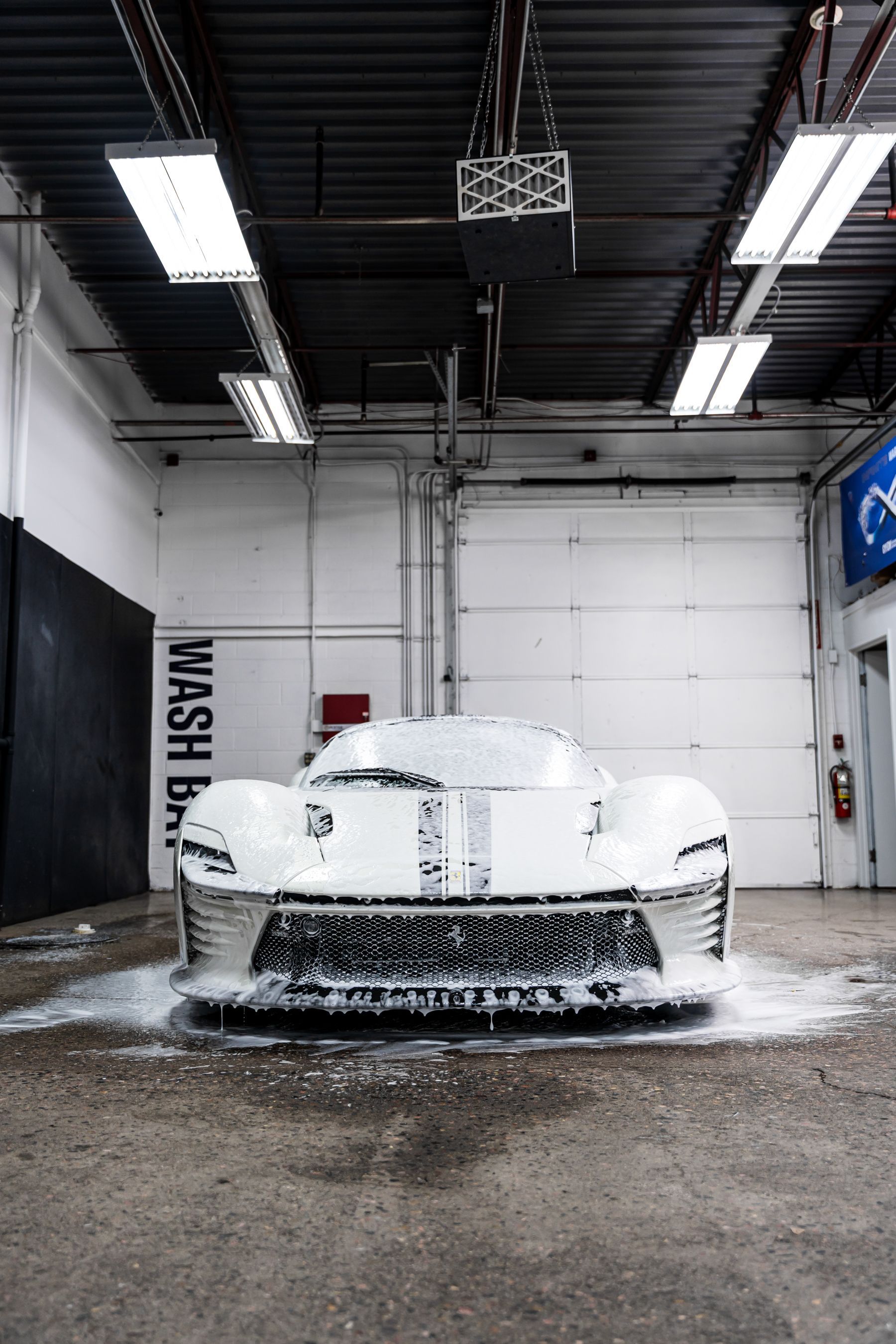 White sports car covered in soap suds at a car wash, ready for cleaning.
