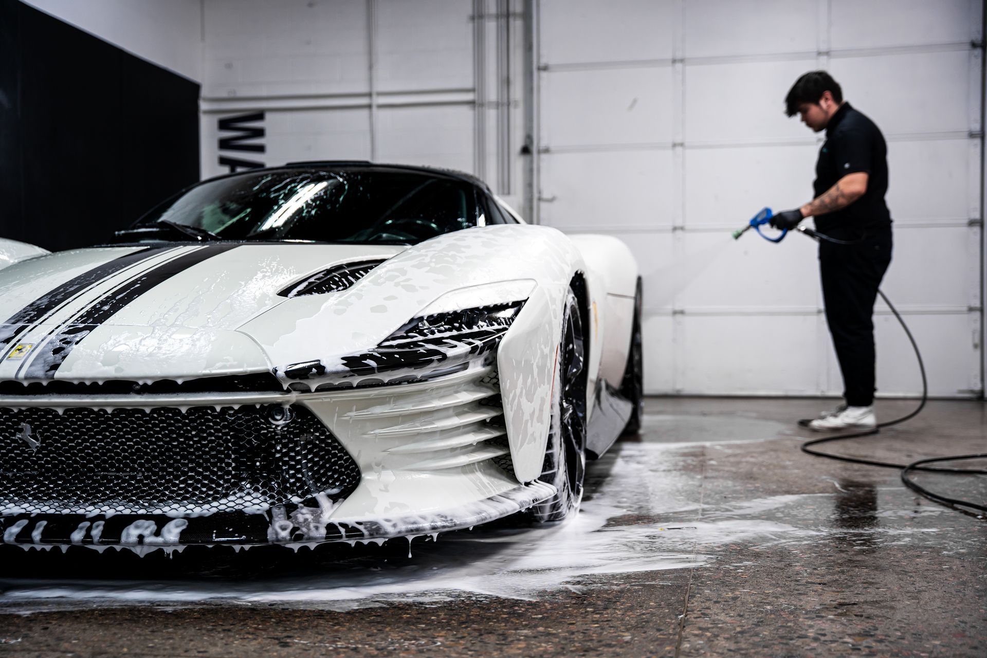 Man washing a white sports car with black stripes in a garage.