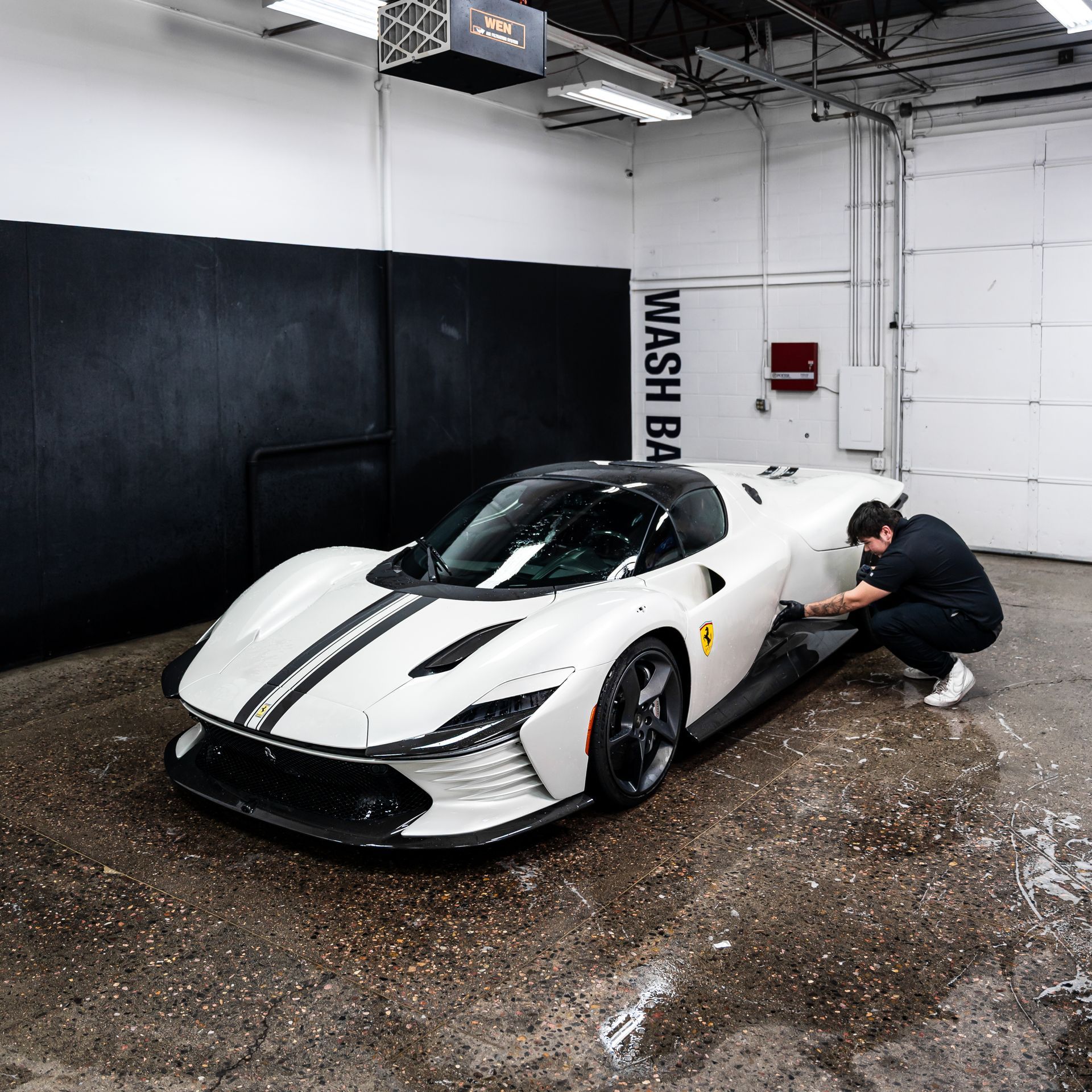 White Ferrari sports car being detailed by a man in a wash bay.