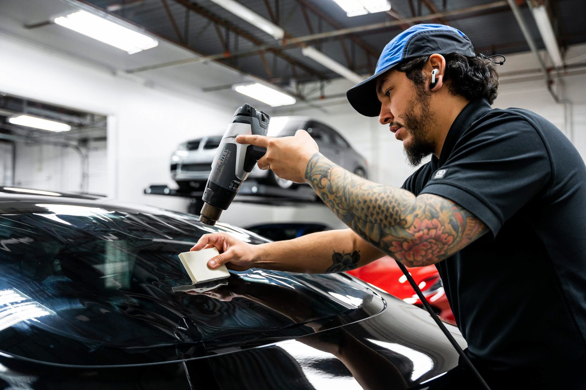 A man is applying window tinting to a car in a garage.