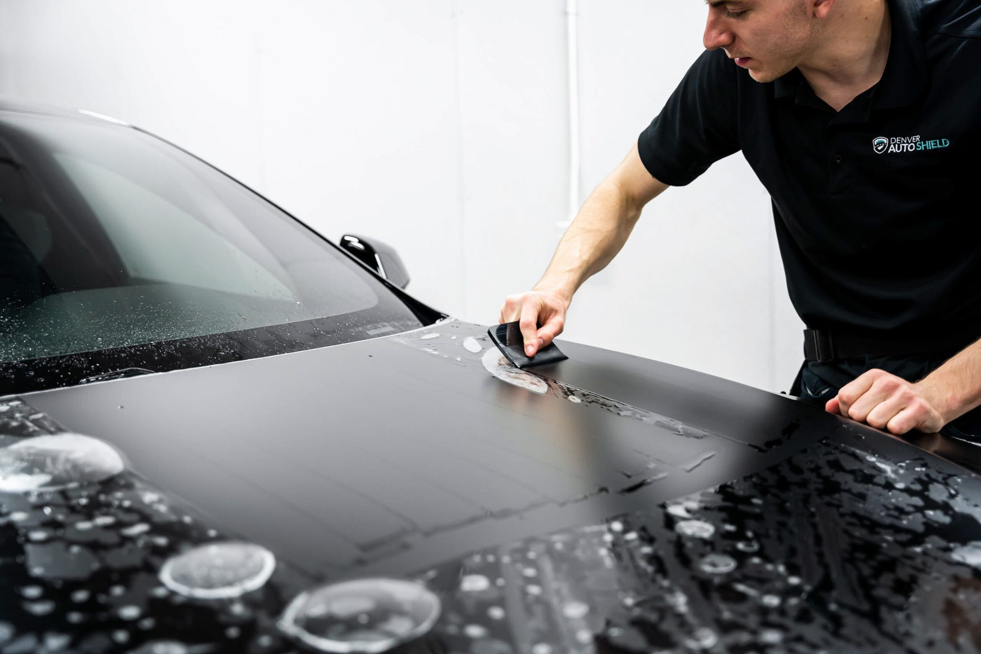 A man is cleaning the hood of a black car.