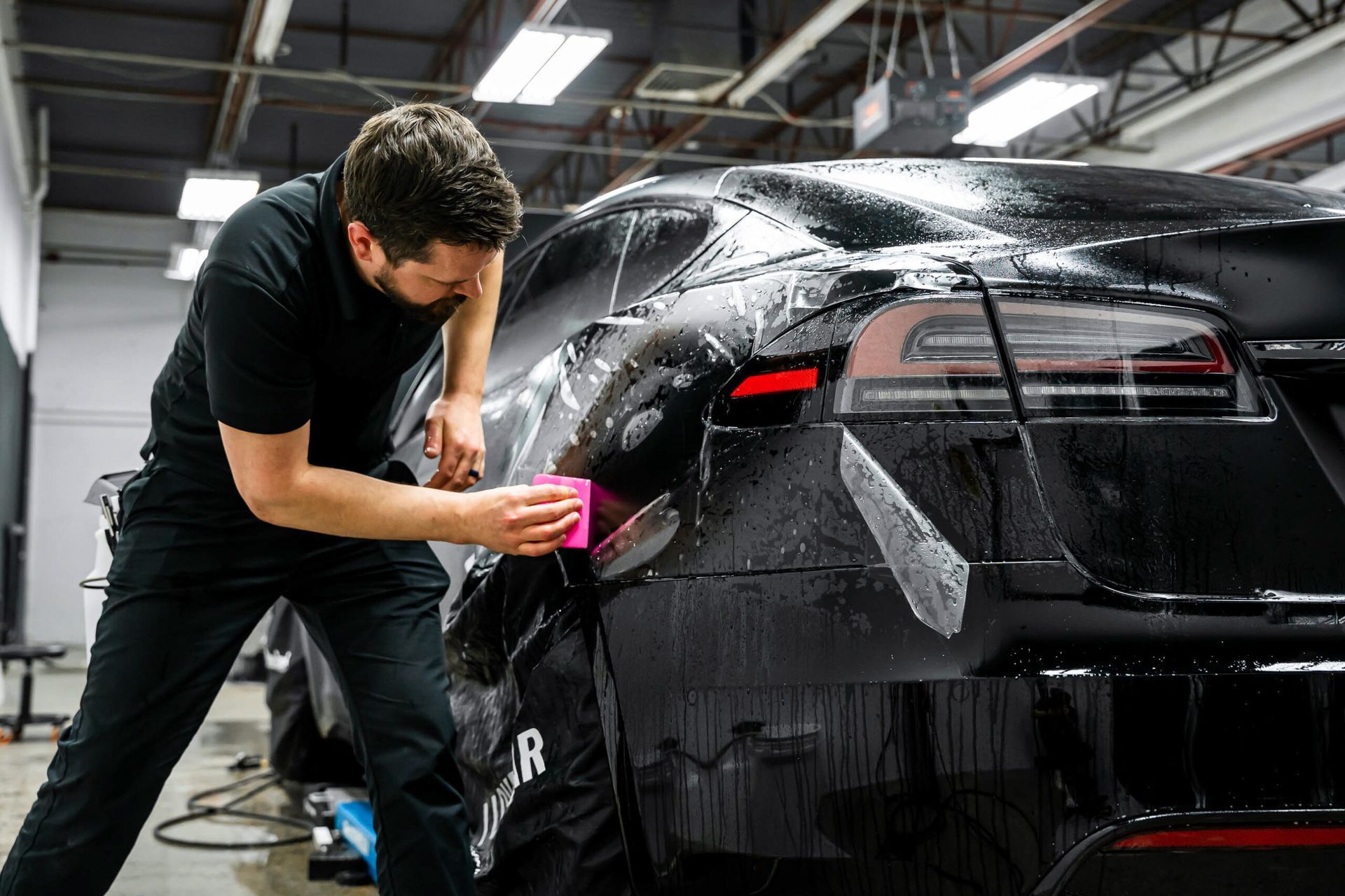 A man is wrapping a black car in a garage.