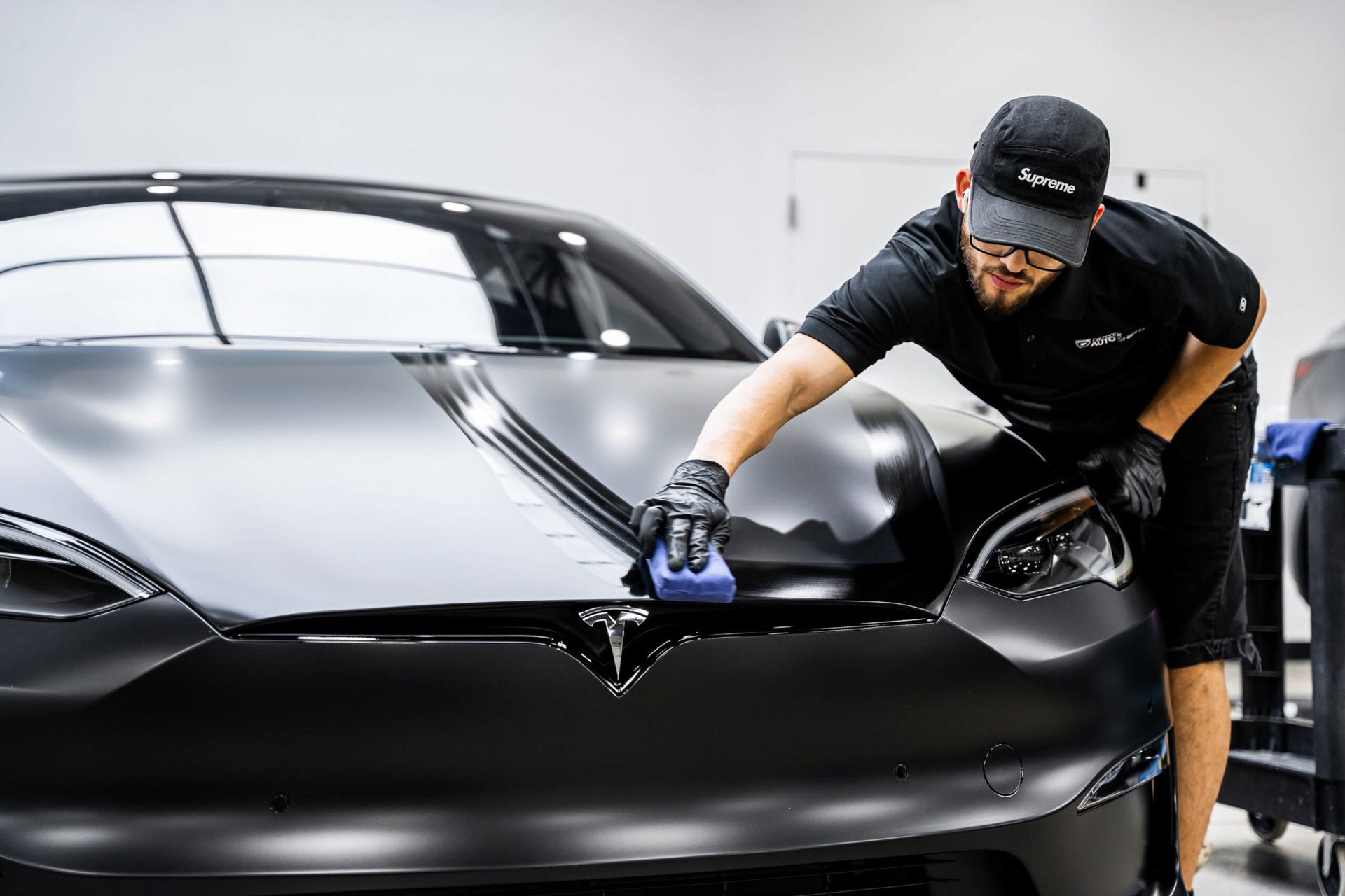 A man is polishing the hood of a black tesla model s.