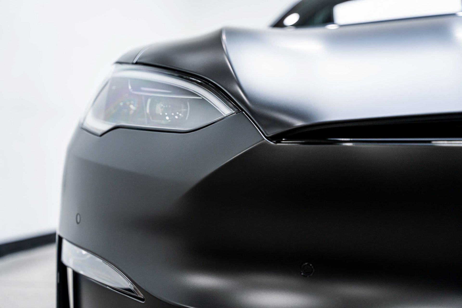 A close up of the headlight of a black tesla model s.