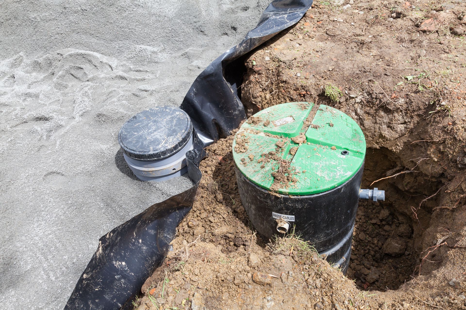 Green and gray utility pipes exposed in a dirt trench beside black waterproof sheeting Green and gray utility pipes exposed in a dirt trench beside black waterproof sheeting