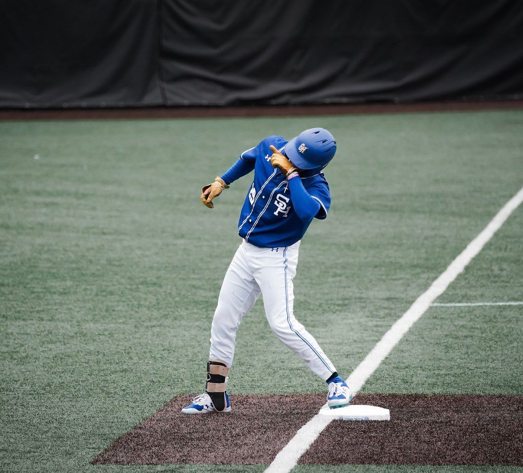 Baseball player in blue uniform swinging at a pitch on an indoor turf field