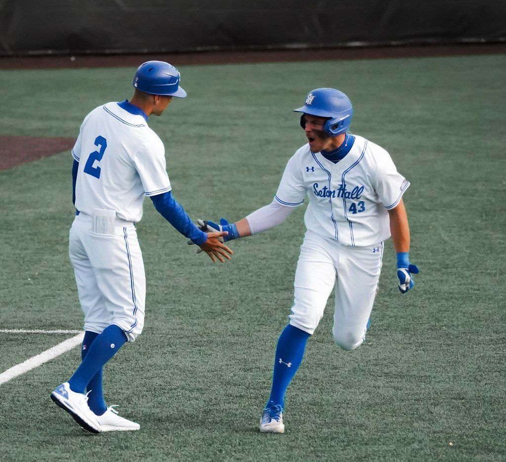 Two baseball players in white and blue uniforms shake hands on the field