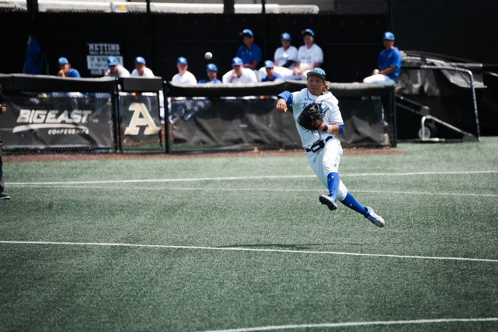 Soccer player in white and blue running on turf field with teammates on the bench behind him