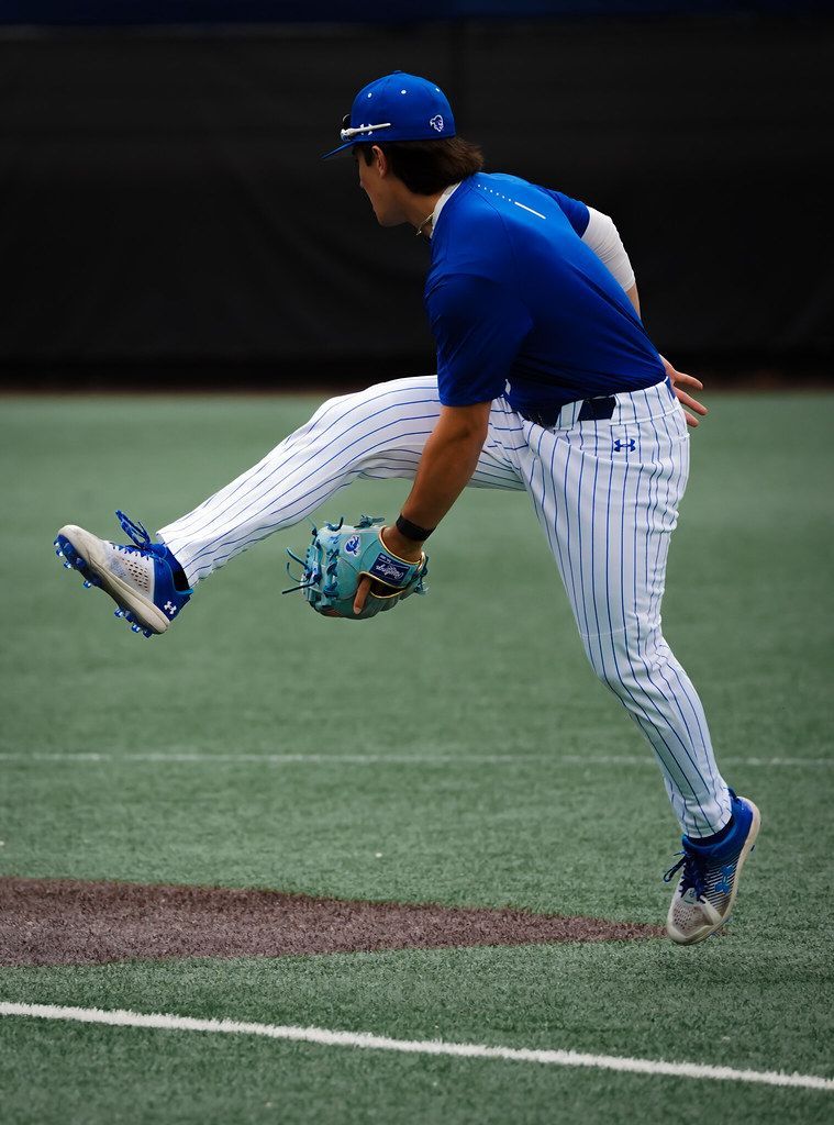 Baseball player in blue uniform mid-pitch on indoor field, leg raised and glove ready