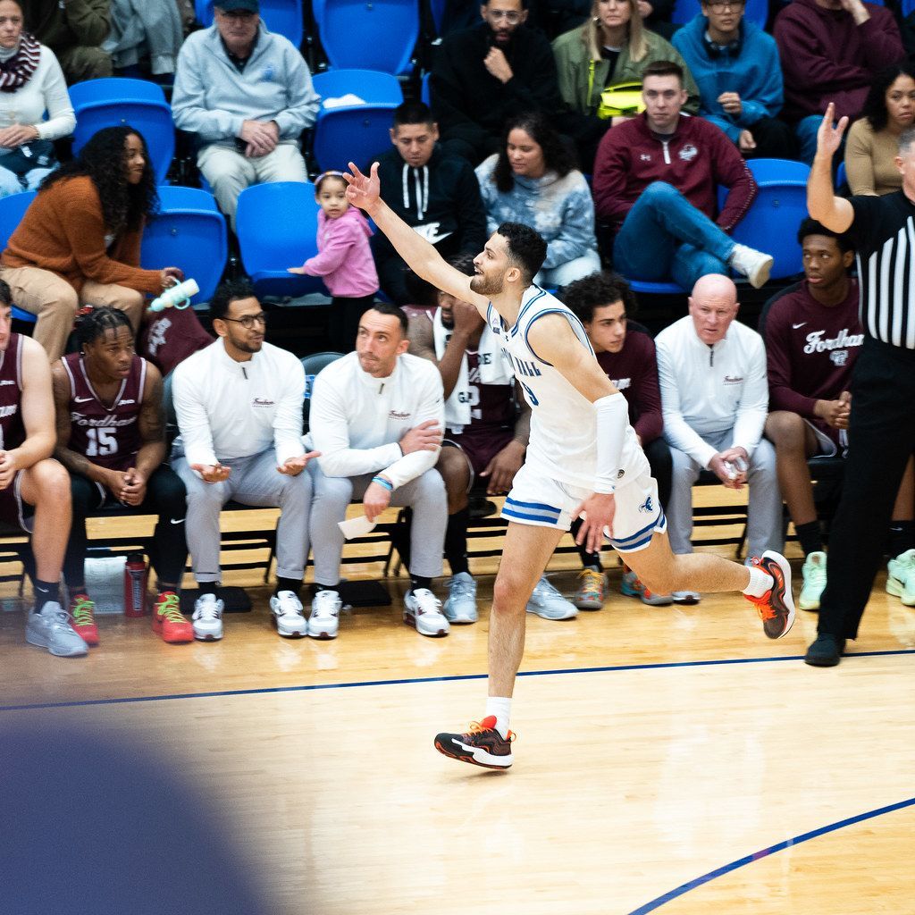 Basketball player in white shoots a jumper near the sideline during a game.