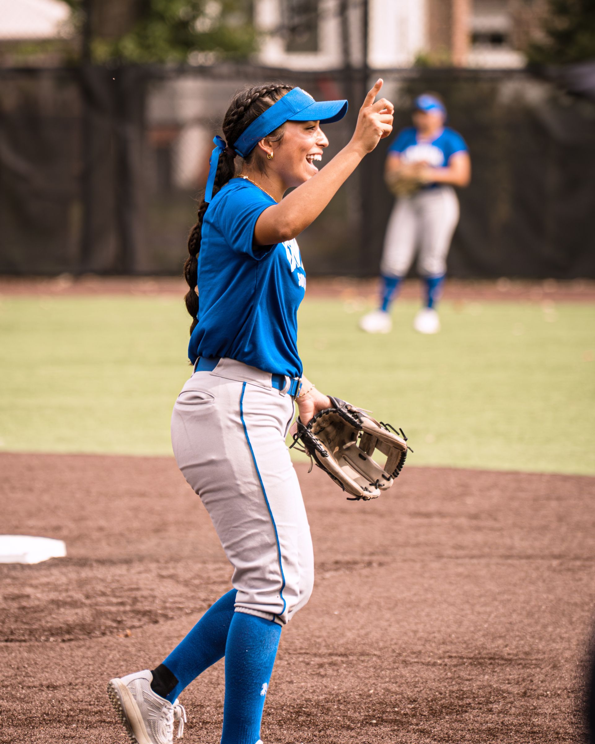 Softball player in blue uniform celebrating on the field with glove raised