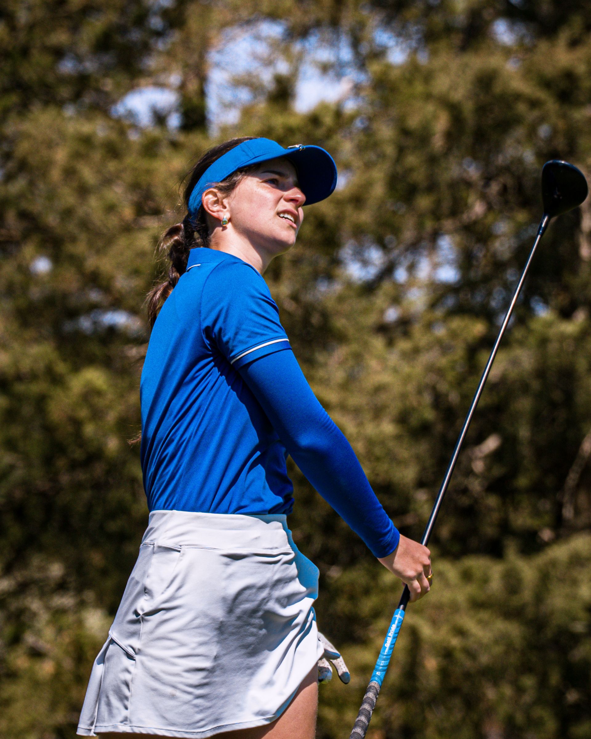 Golfer in blue shirt and cap holding a club on a sunny course