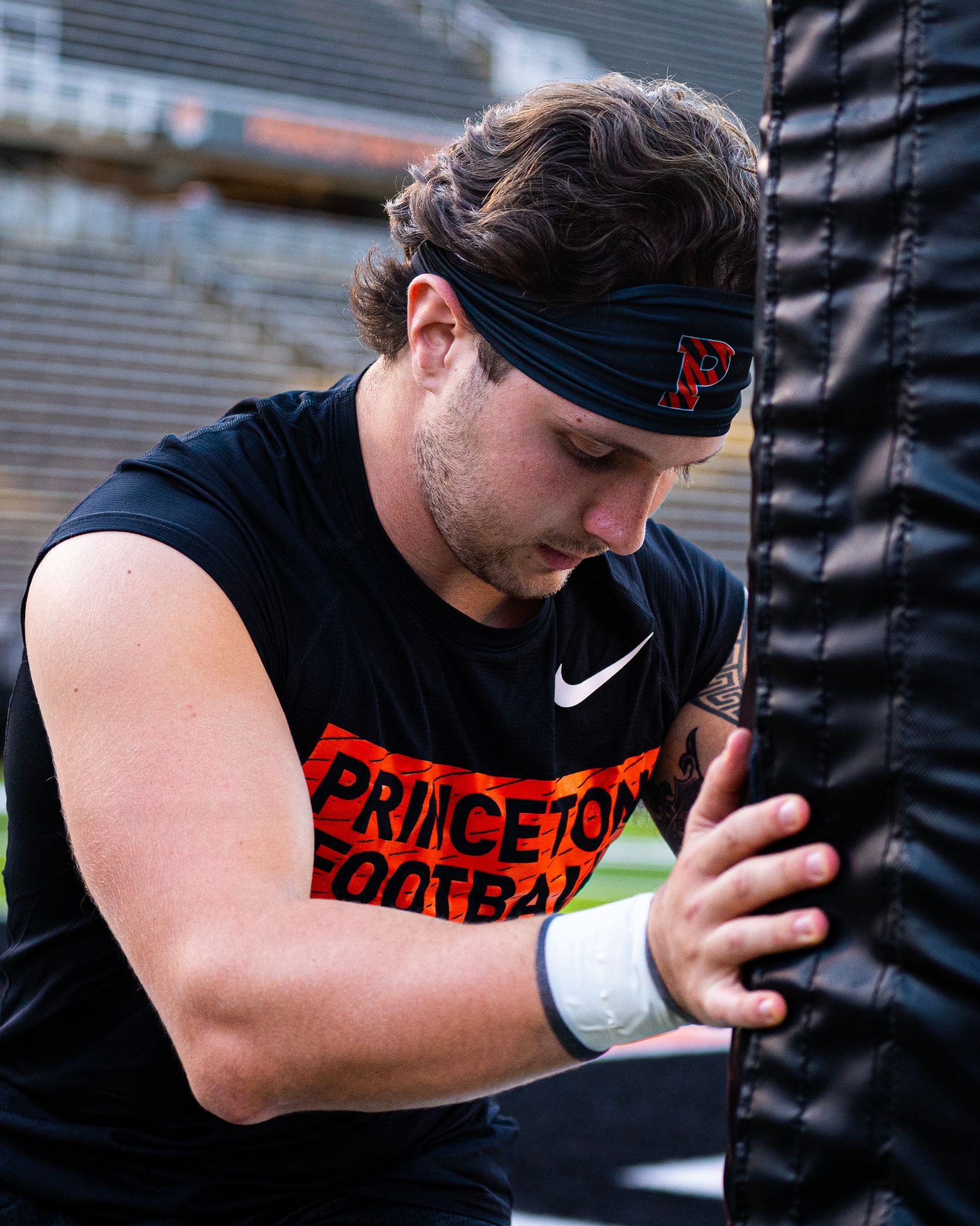 Football player in black Princeton shirt and headband gripping a padded post during practice