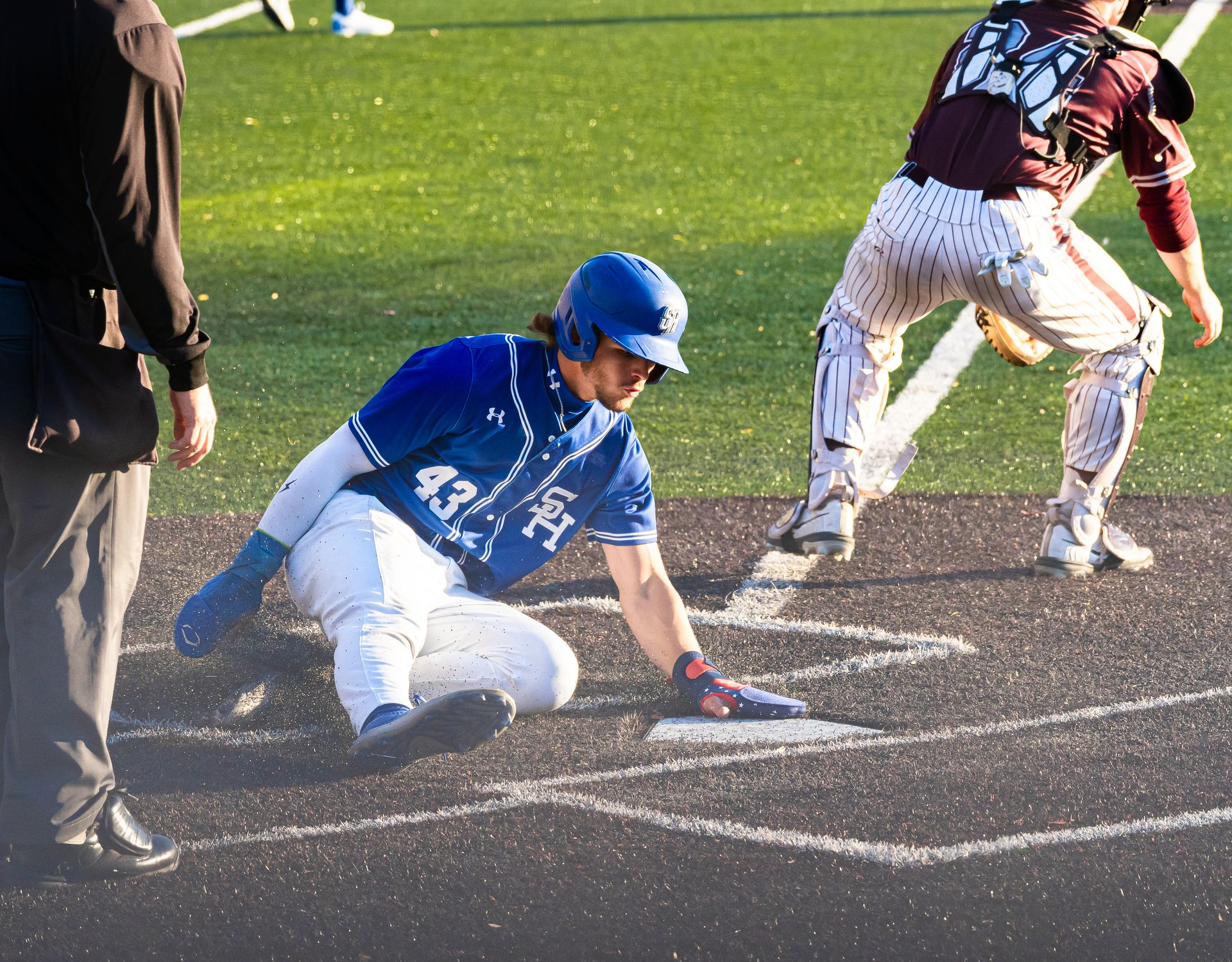 Baseball player in blue slides into a base as the catcher in white prepares to tag him.