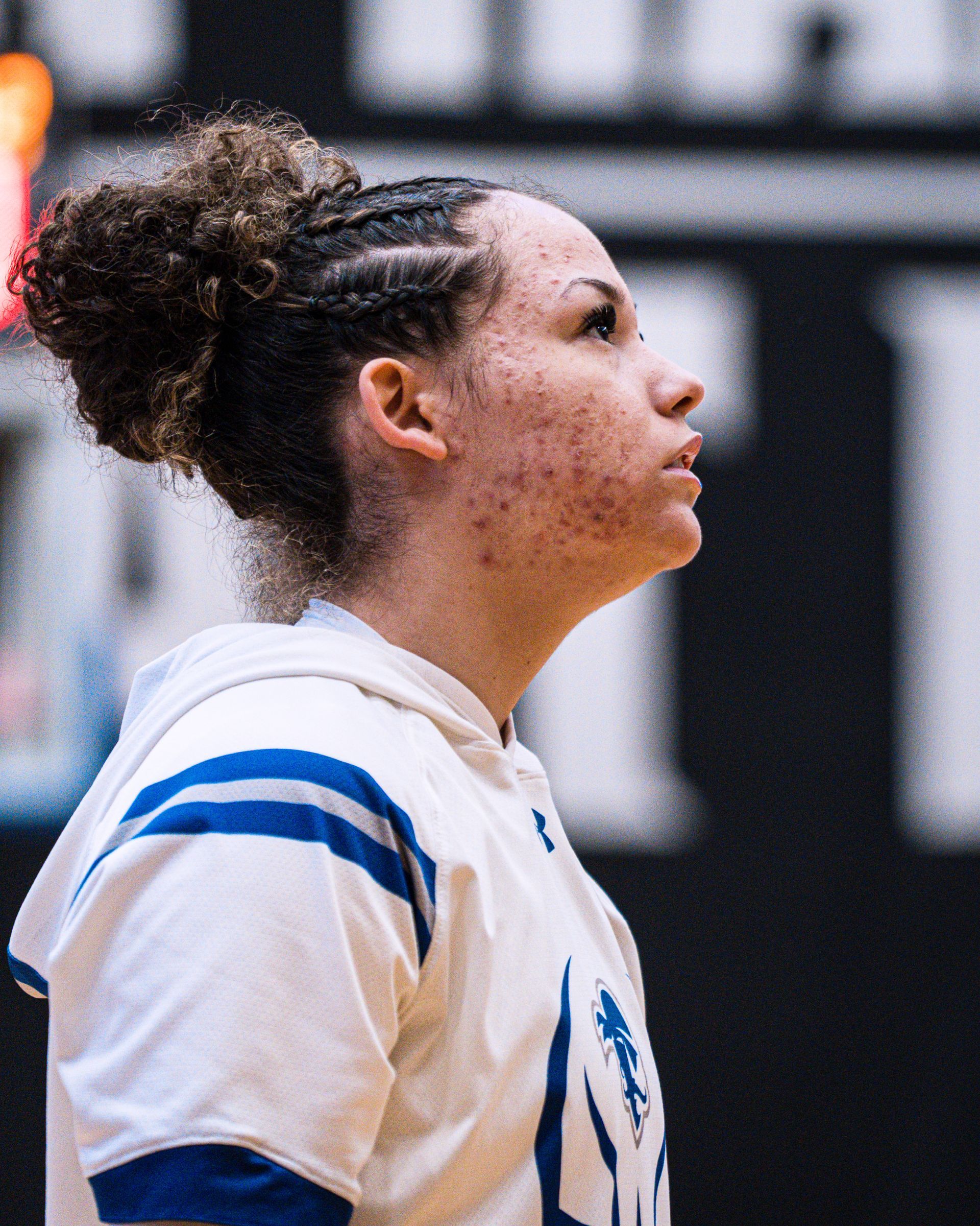 Basketball player in white jersey with blue stripes, shown in profile on the court.