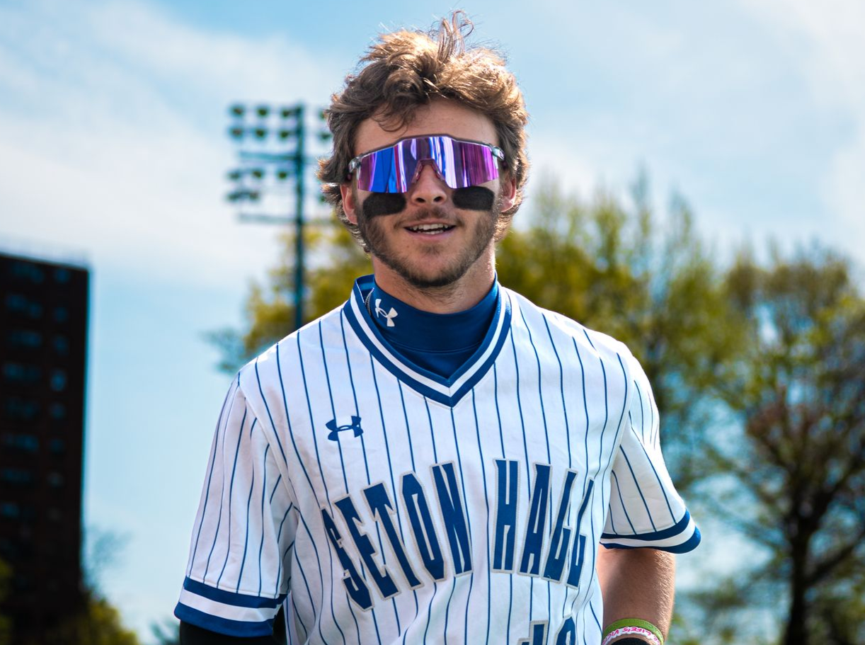 Baseball player in white pinstripe jersey and mirrored sunglasses standing outdoors in sunlight