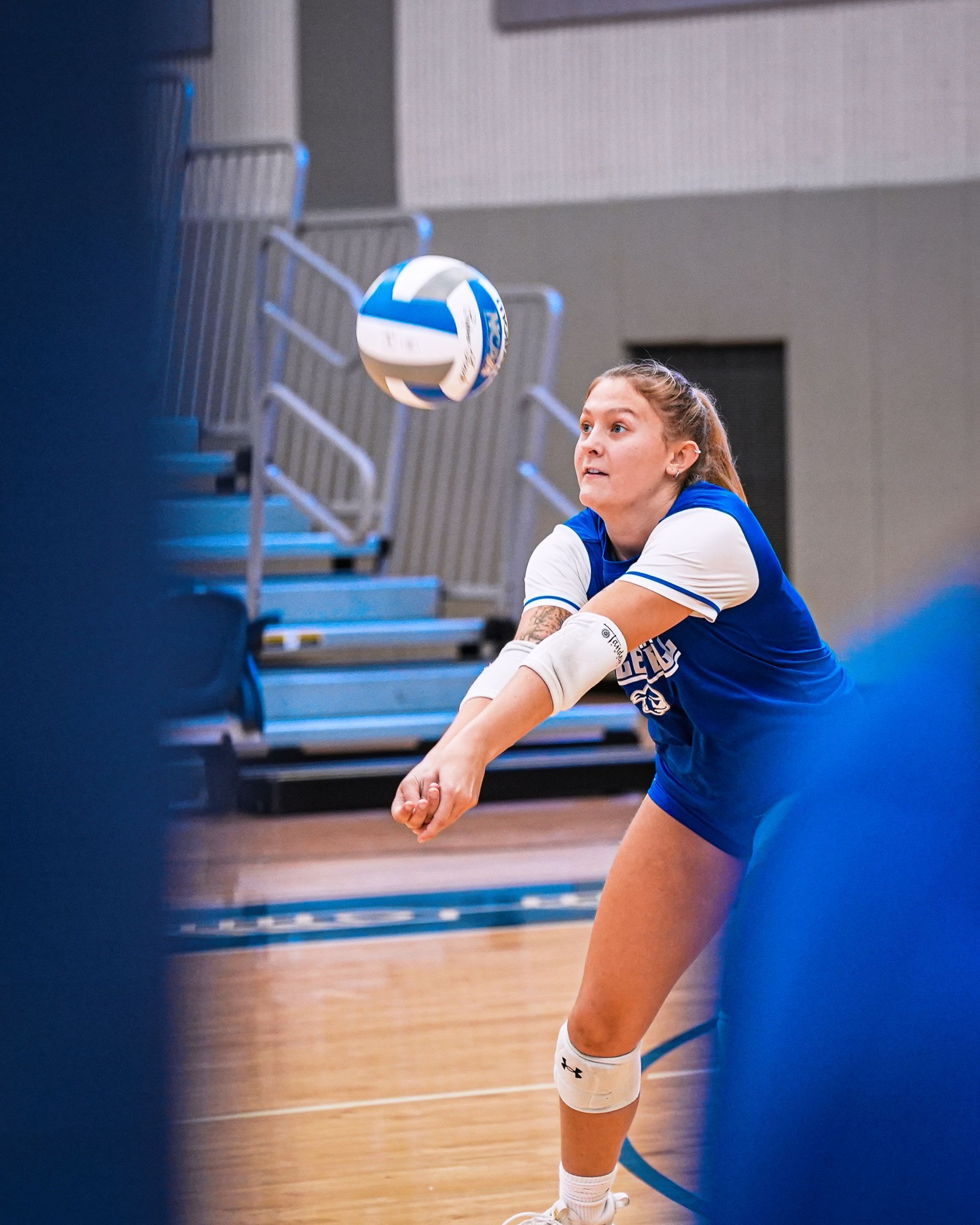 Volleyball player in blue jersey bumping a ball on an indoor court