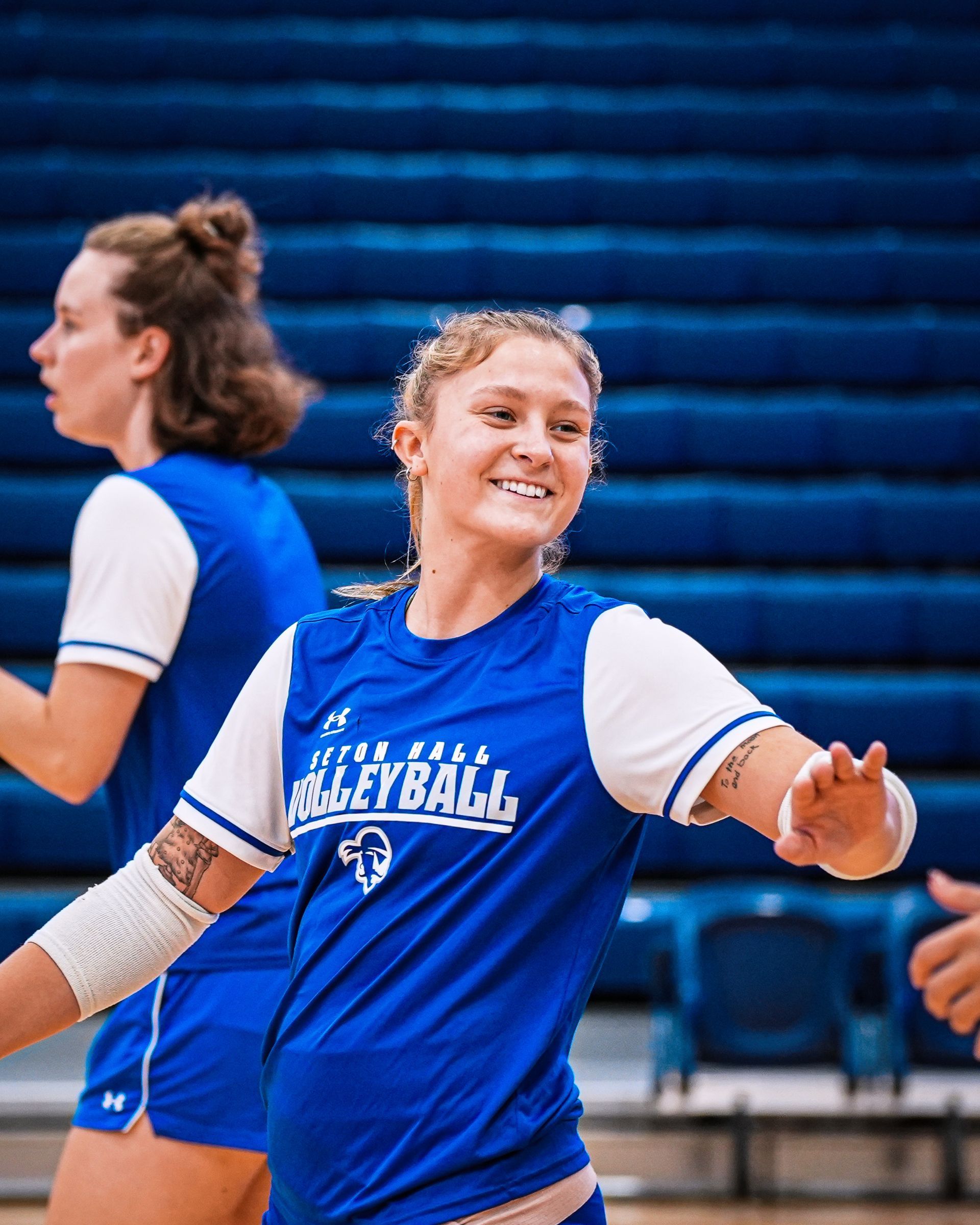 Volleyball player in blue jersey smiles and gestures on court during practice