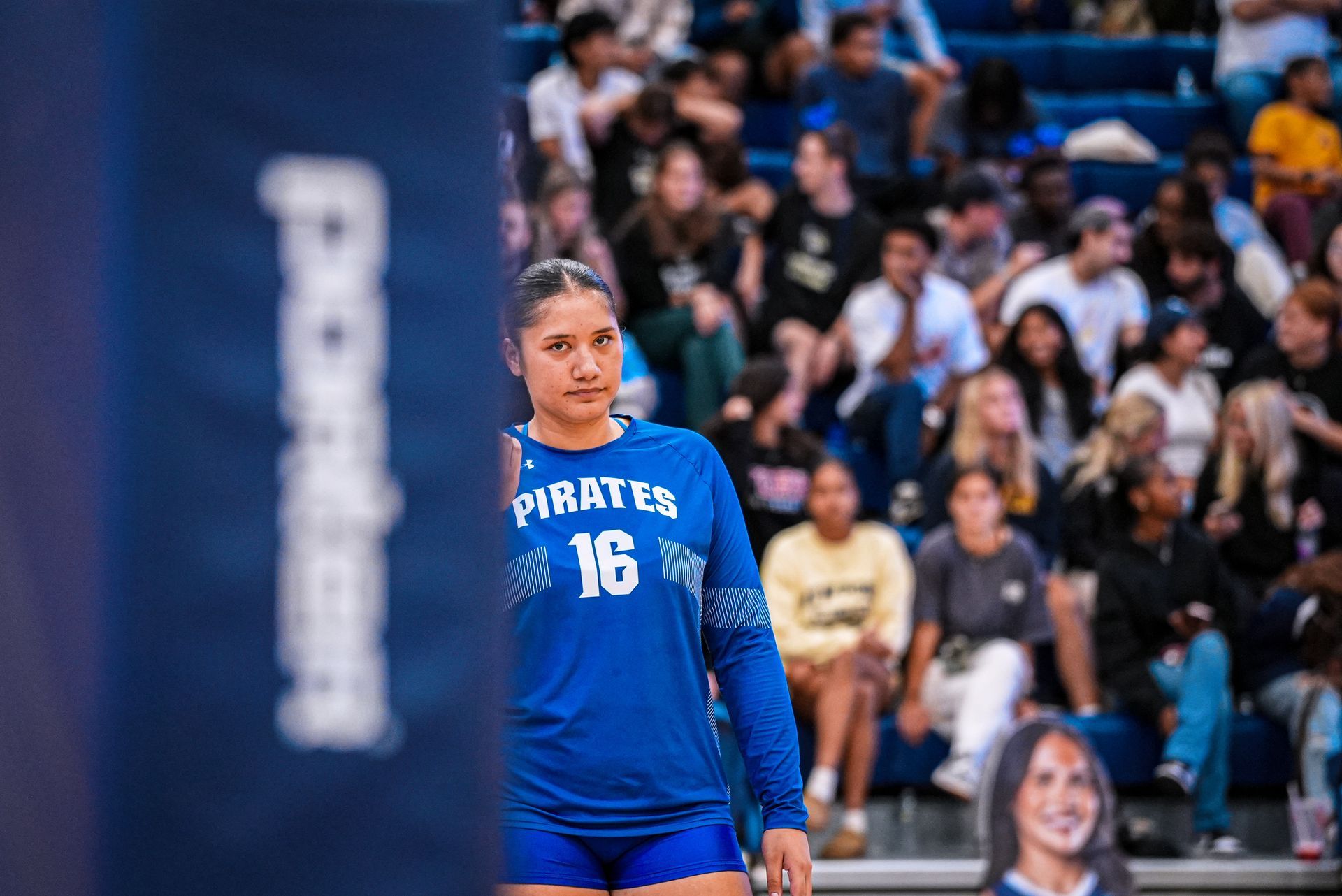 Female athlete in blue uniform stands on the court before a cheering crowd