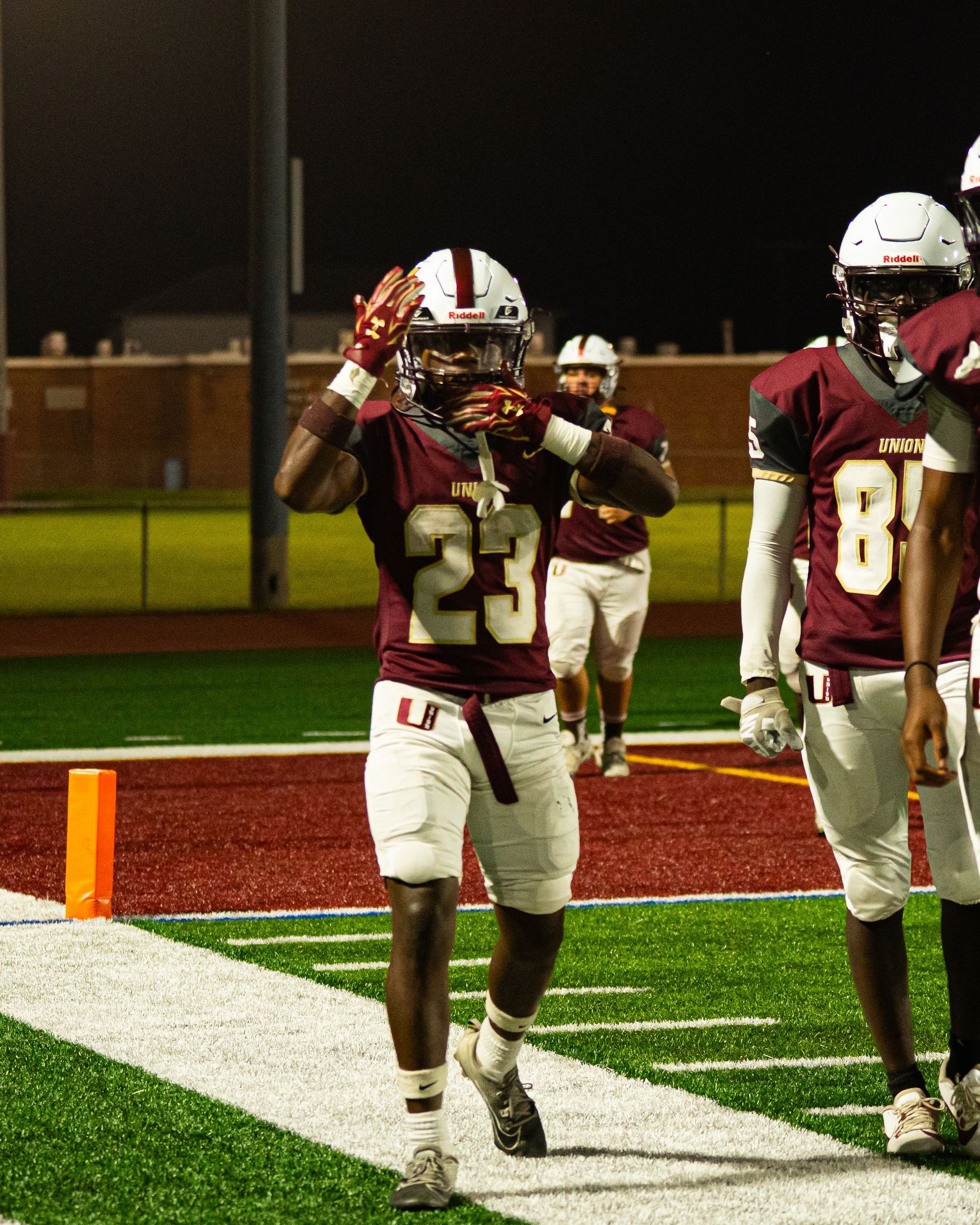 Two football players in maroon jerseys celebrate in the end zone at night.