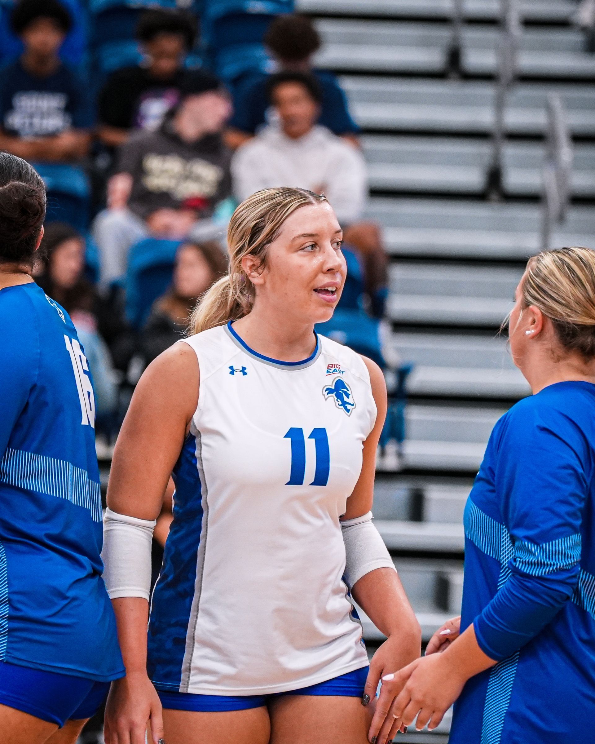 Volleyball player in white jersey number 11 talks with teammates on the court