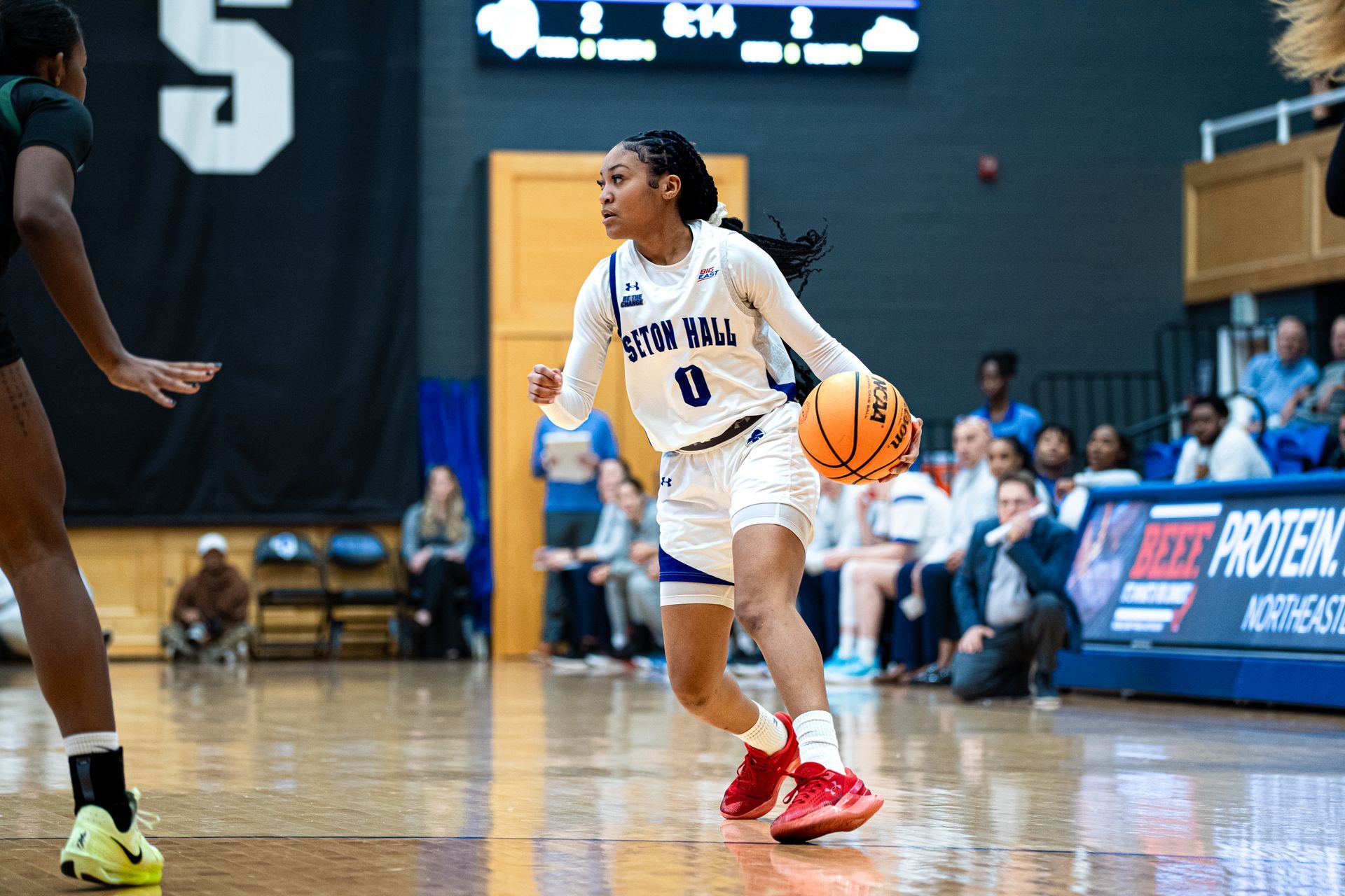 Basketball player in white dribbles an orange ball on a gym court during a game