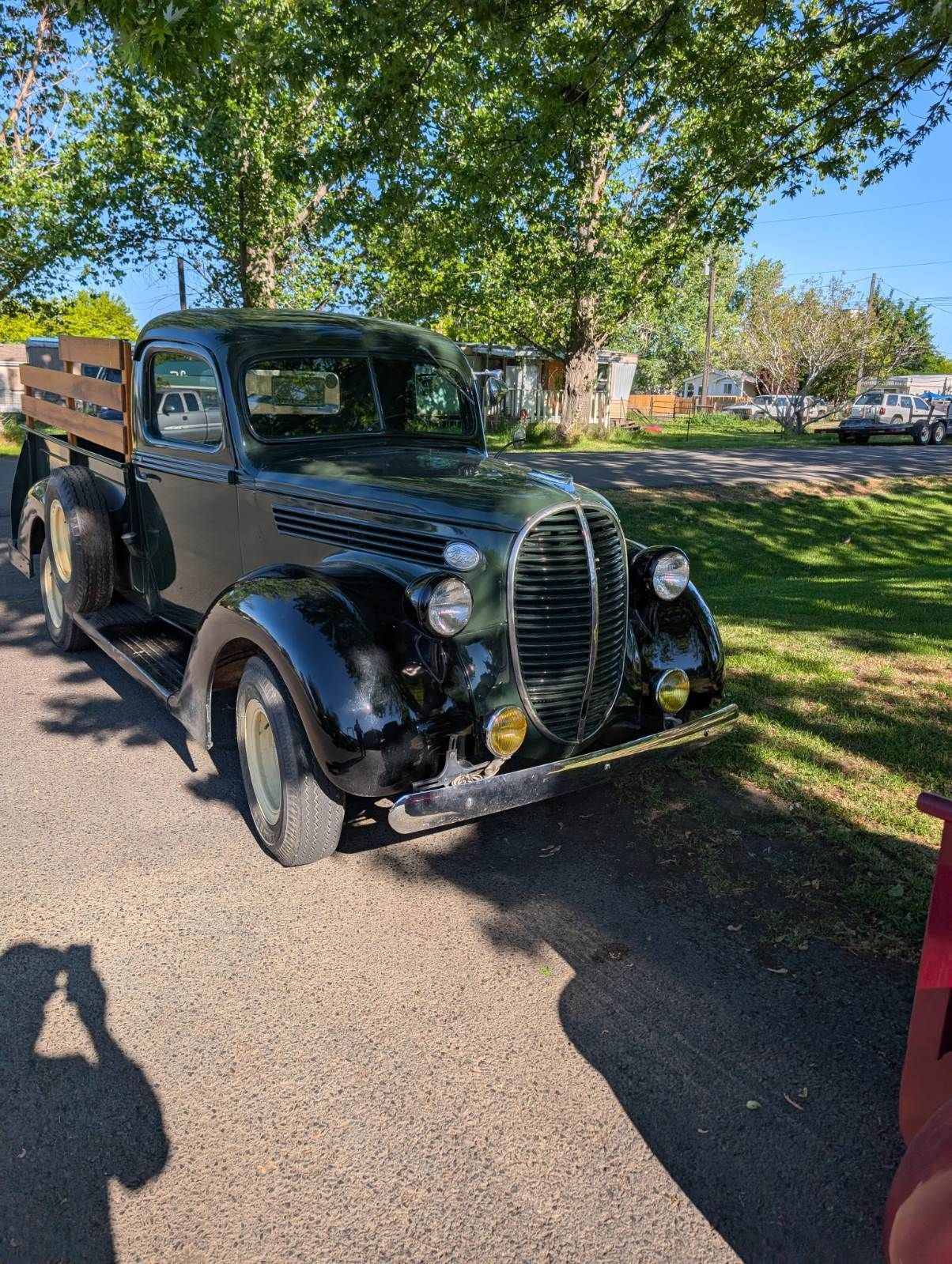 Vintage black pickup truck parked on a sunlit driveway under trees