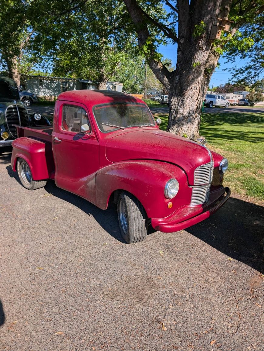 Red vintage pickup truck parked under trees in a lot on a sunny day