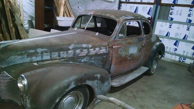 Rusty vintage car in a workshop, partially restored and covered in primer.