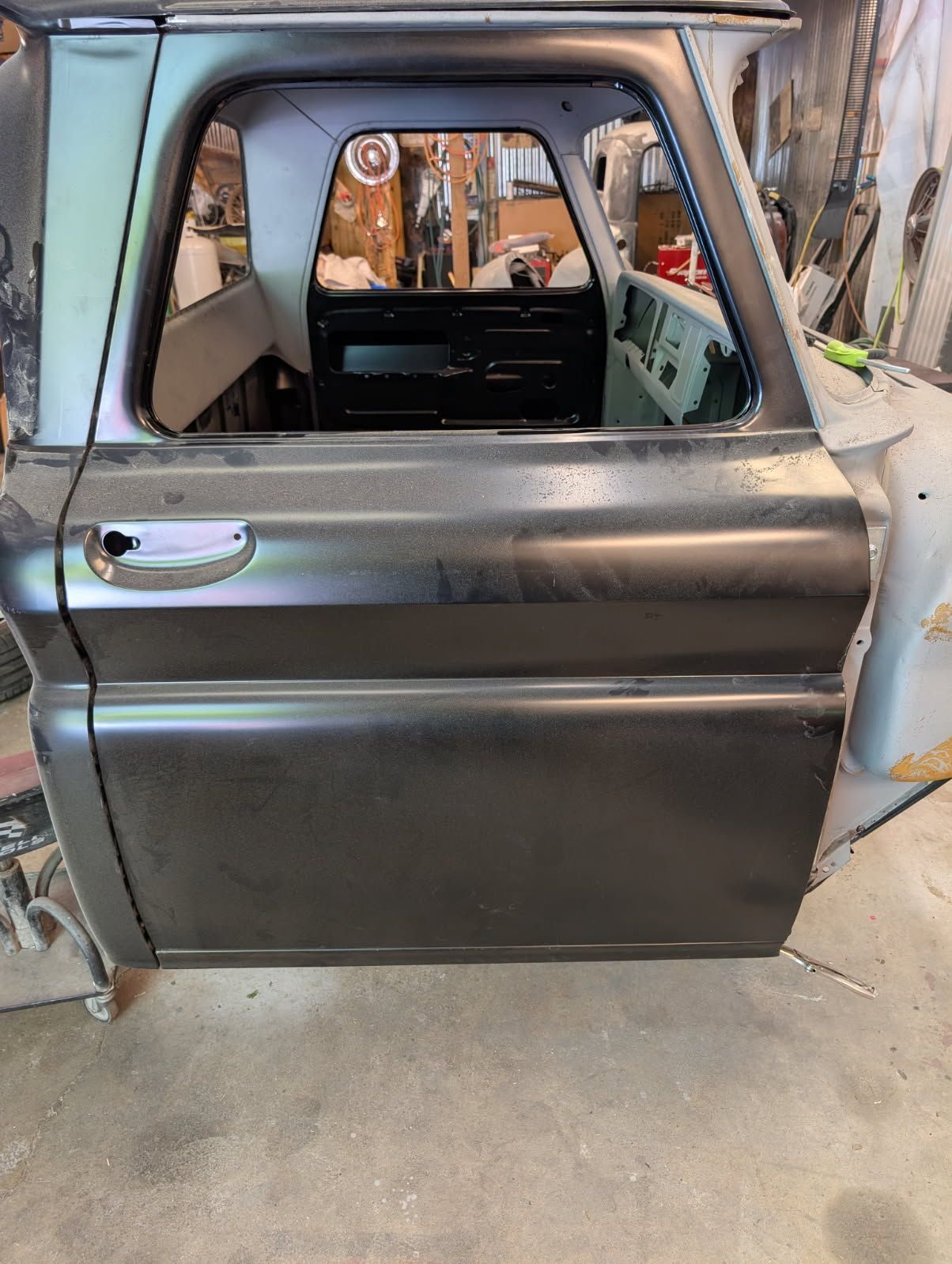 Silver truck cab with a dented door and missing window, shown in a garage during repair.