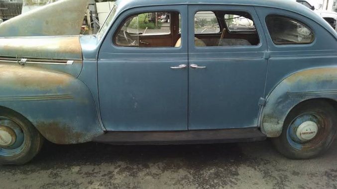 Side view of a faded blue vintage sedan parked on a dirt road.