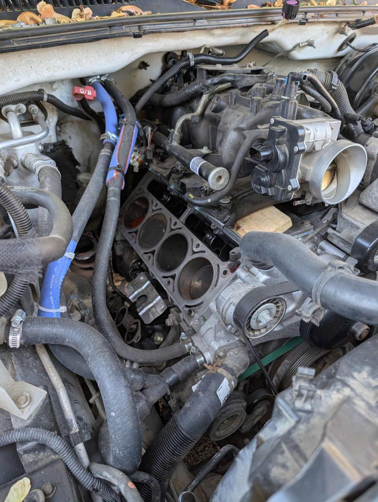 Destroyed car engine compartment with exposed black intake manifold and tangled hoses