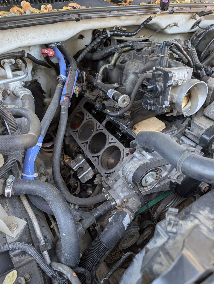 Destroyed car engine compartment with exposed black intake manifold and tangled hoses