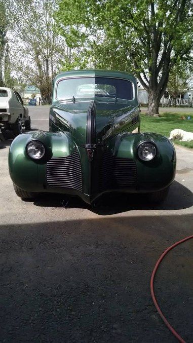 Front view of a dark green vintage car parked outdoors under trees