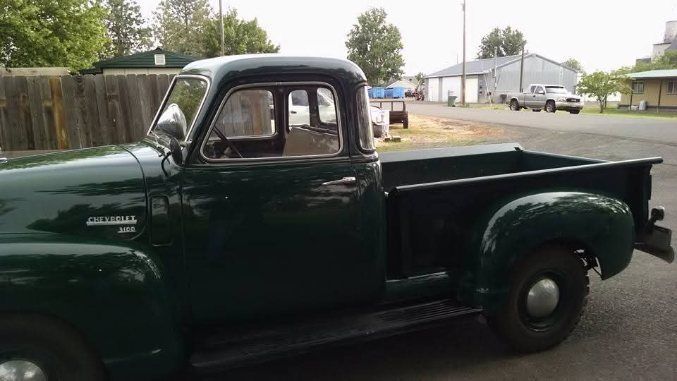Dark green vintage pickup truck parked on a residential street, side view.
