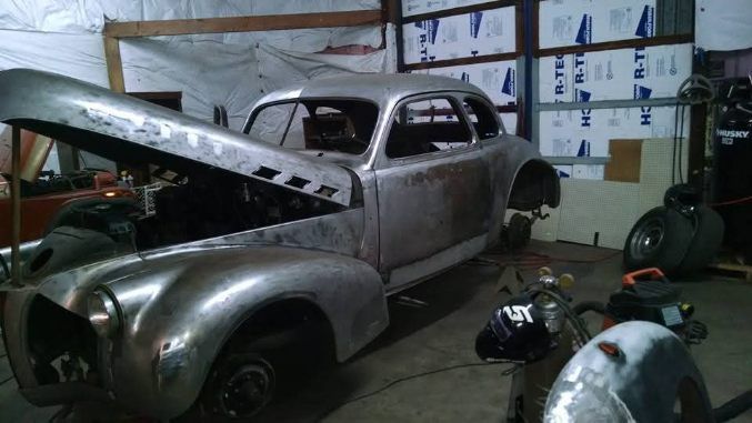 Old gray classic car undergoing restoration in a garage, hood open with tools and parts nearby