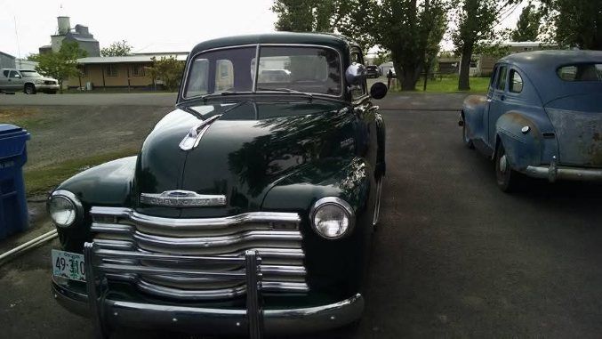 Classic dark green vintage car parked outdoors beside a blue car.