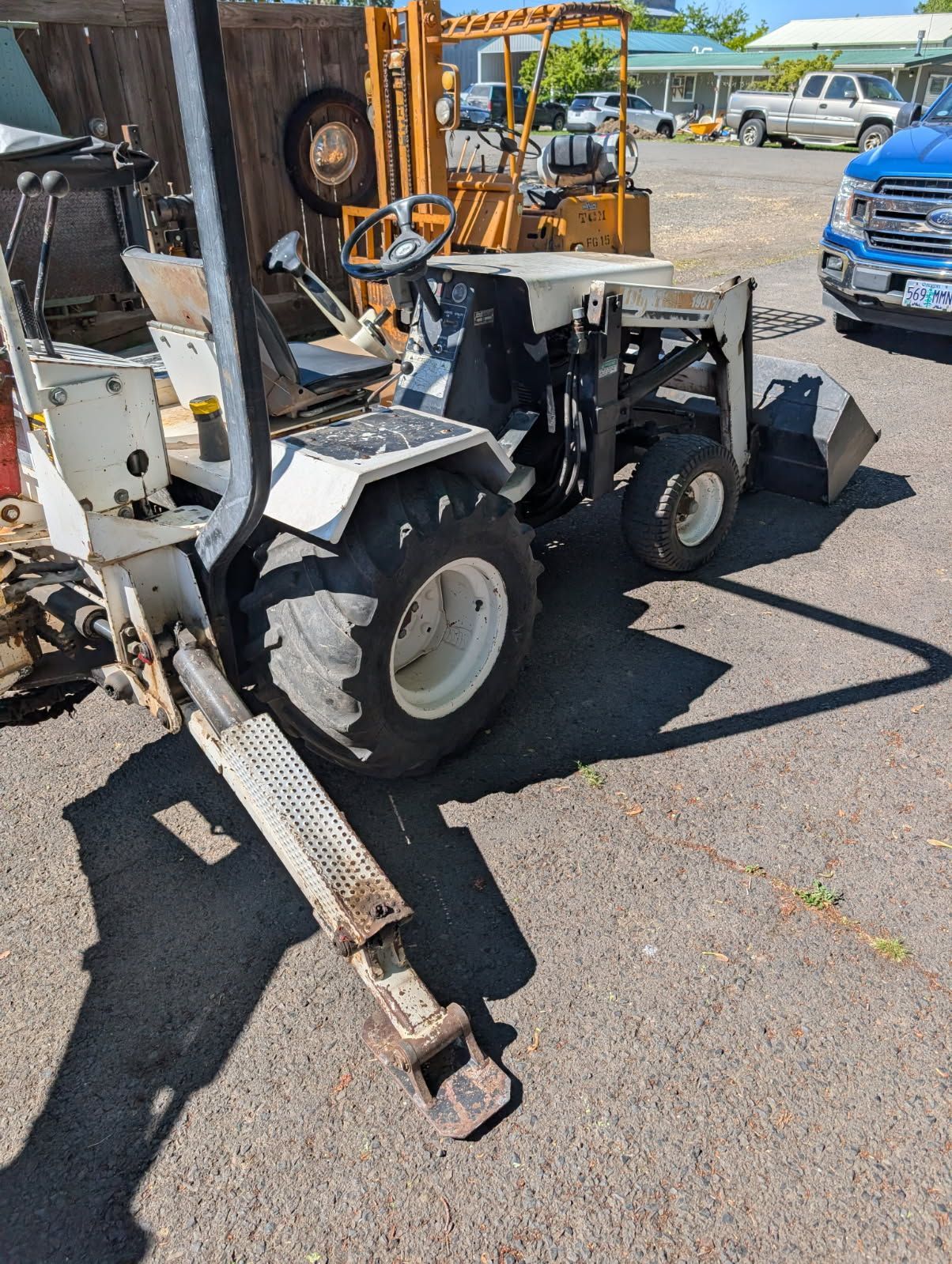 Compact construction machine with white and black tires parked outdoors near other equipment.