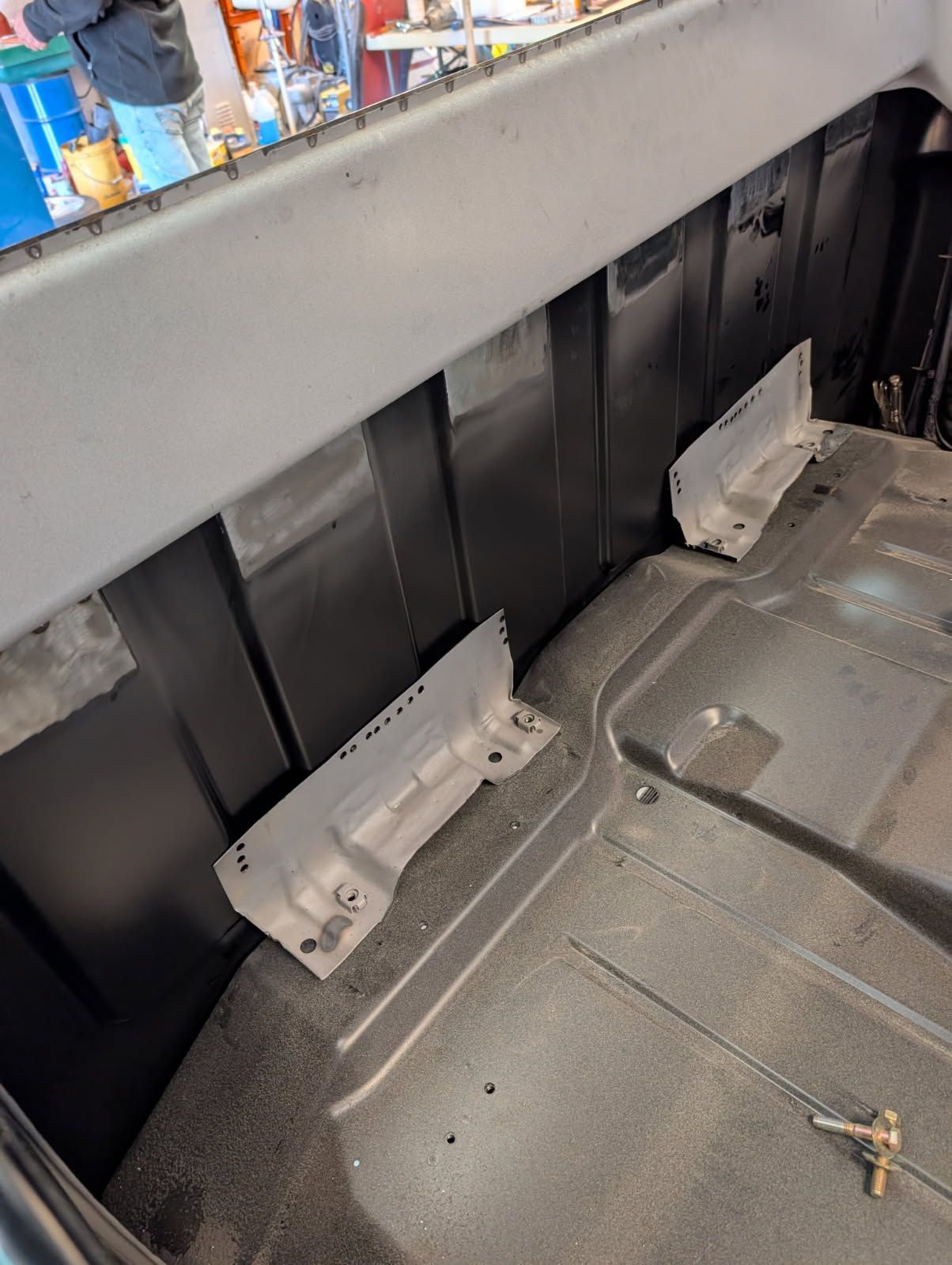 Damaged car trunk interior with torn black paneling, gray trim, and loose metal hardware on the floor.