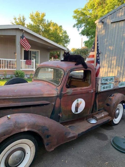 Rusty vintage pickup truck with flags parked beside a building in a driveway