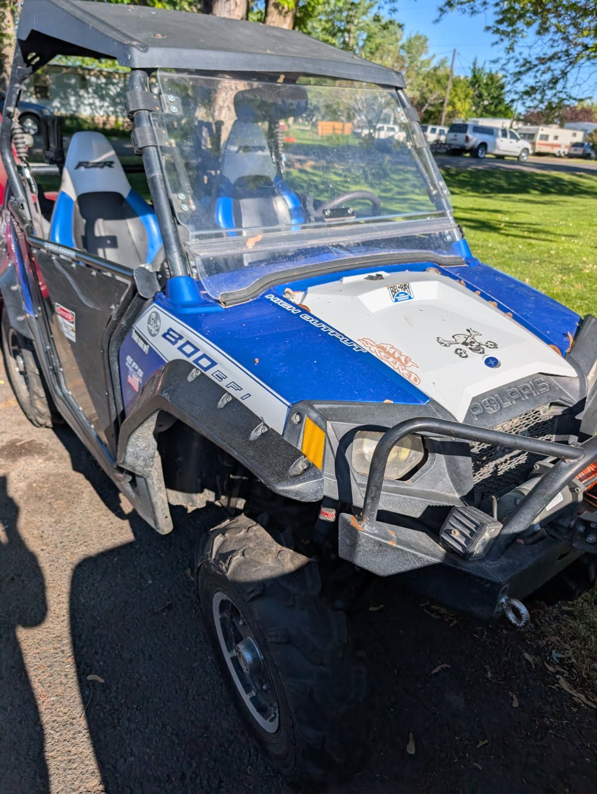 Blue-and-white off-road utility vehicle with damaged front end parked on a street