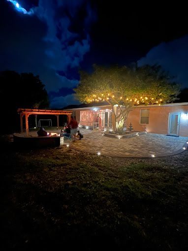 A house is lit up at night with a fire pit and a tree.