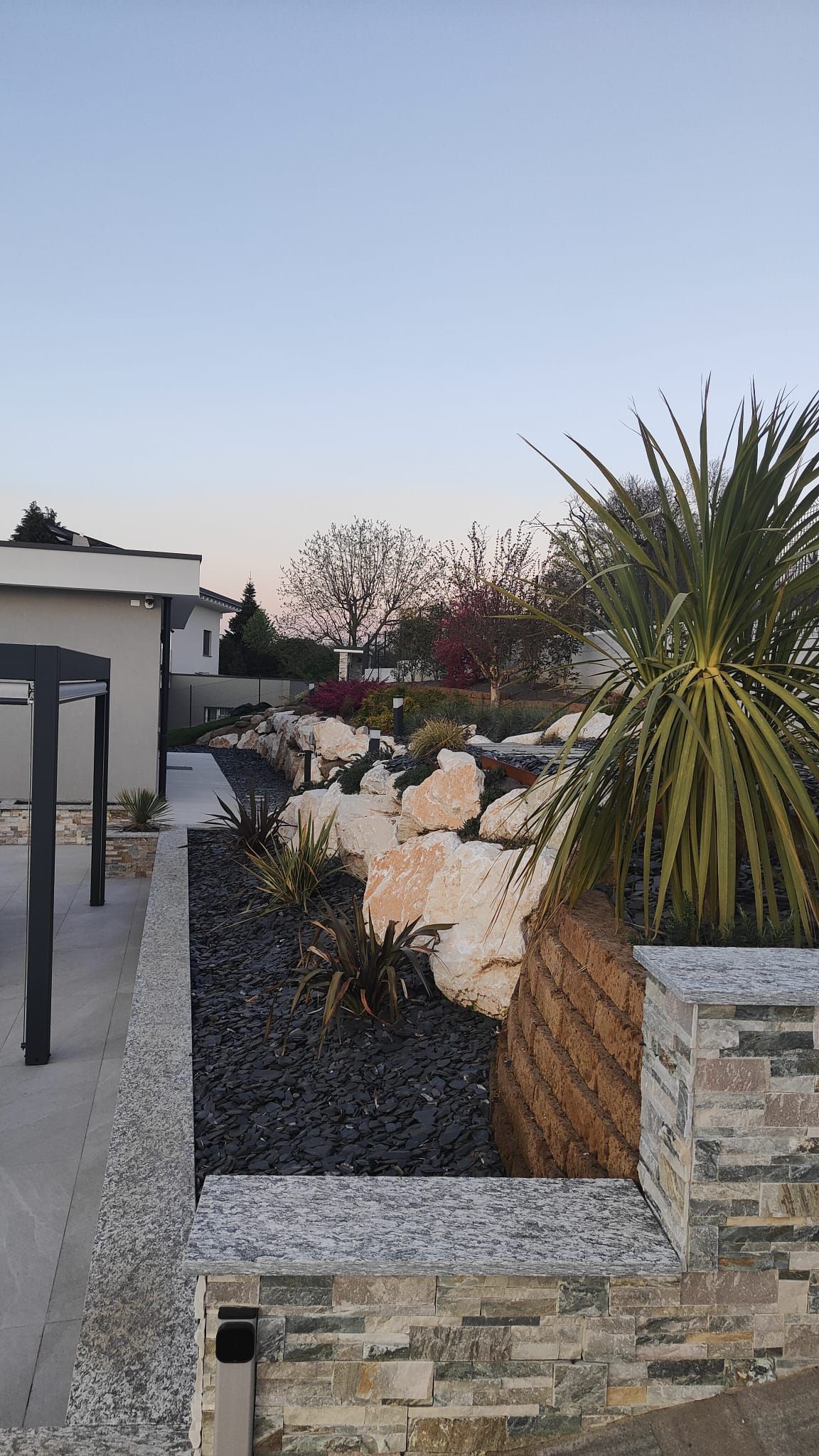 Giardino anteriore curato con piante del deserto, fioriere in pietra e una casa moderna al crepuscolo