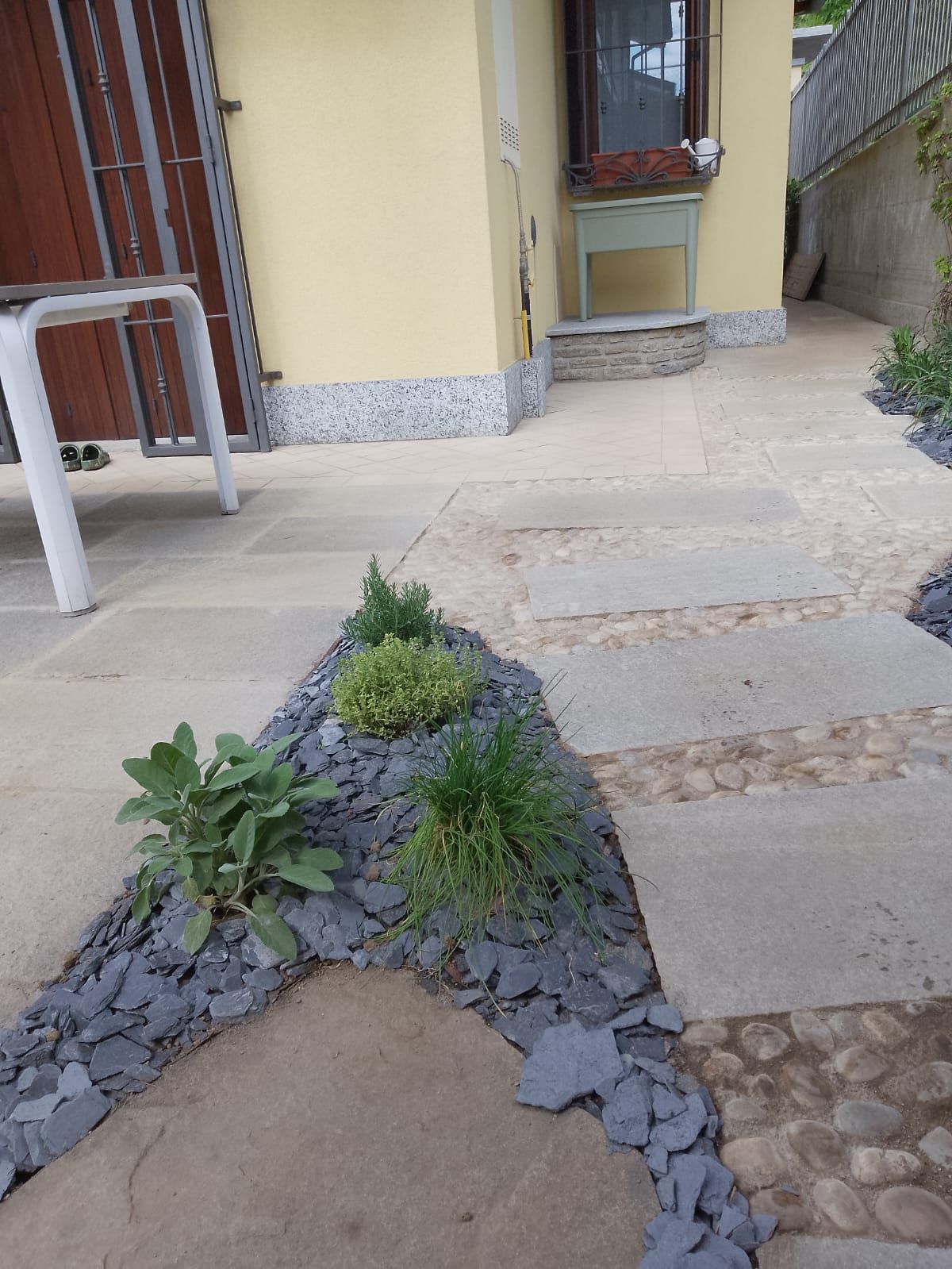 Un vialetto di pietra accanto alla casa, con piccole piante in un letto di ghiaia e una sedia bianca sulla sinistra.