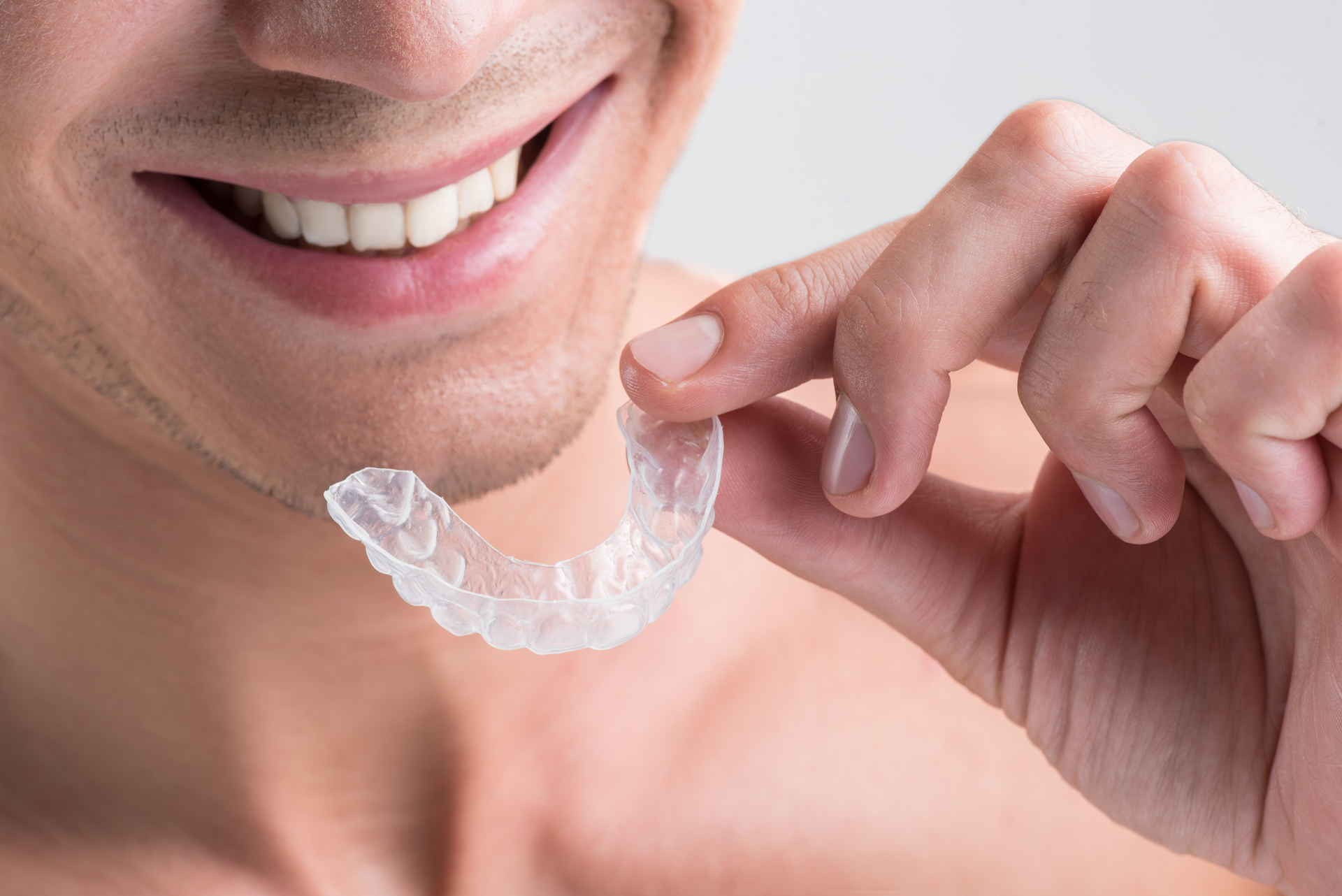 Person holding clear dental aligner near mouth to show teeth straightening device for smiles perfect.